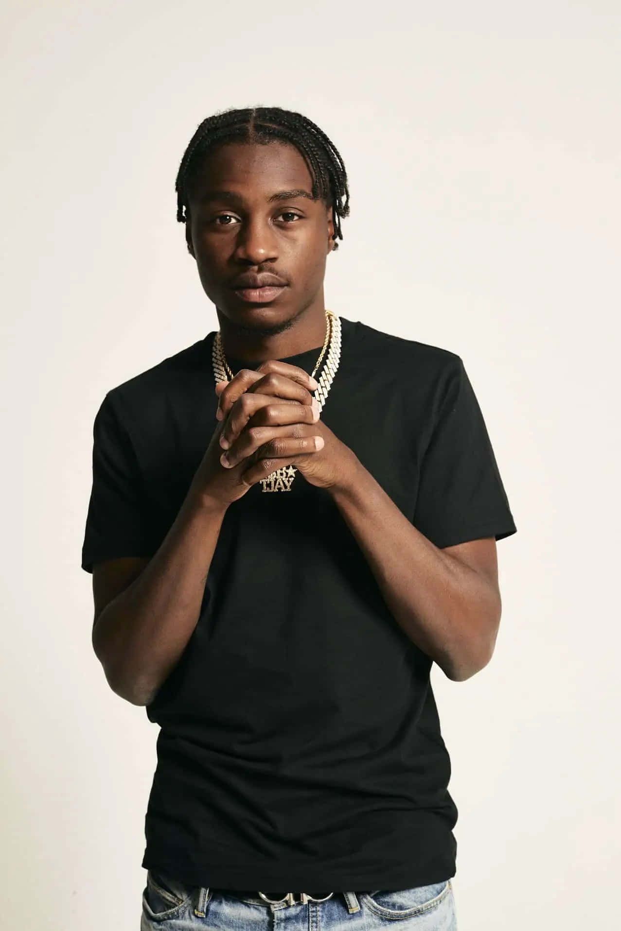Lil Tjay 桌布 壁紙 — 一位辮子頭髮的年輕男子穿著黑色T恤和金色鏈條，在純白背景前雙手合十。