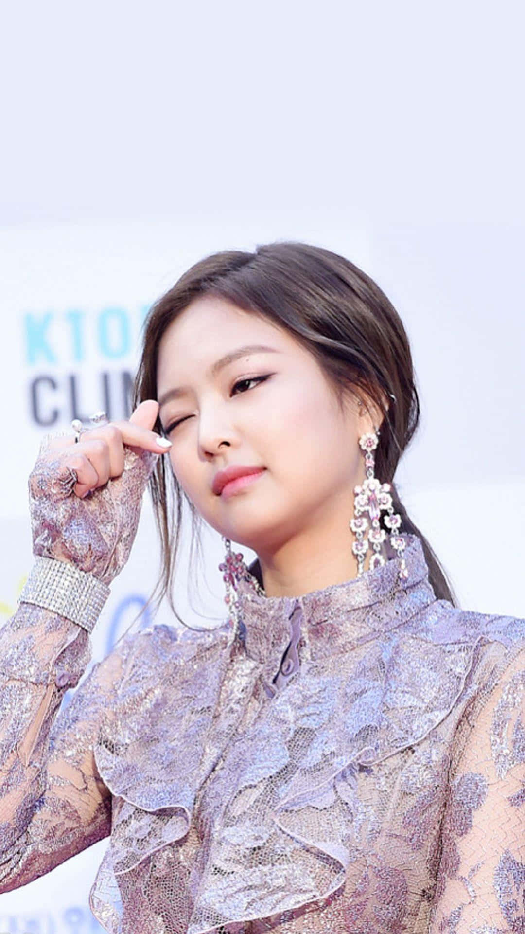 Jennie Kim 桌布 壁紙 — 一位迷人女士身穿閃爍薰衣草蕾絲服裝，戴著閃亮吊燈耳環，俏皮地眨眼。