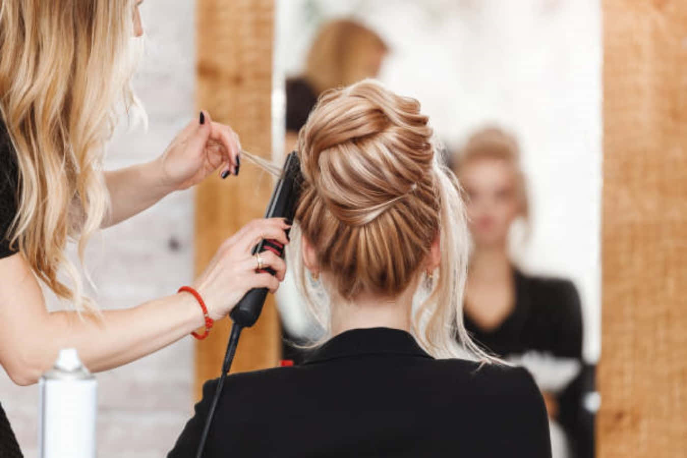 Hair Salon 桌布 壁紙 — 一位造型師在光線充足、帶有木質裝飾的沙龍中，為一位金髮客戶複雜的盤髮使用直髮夾。