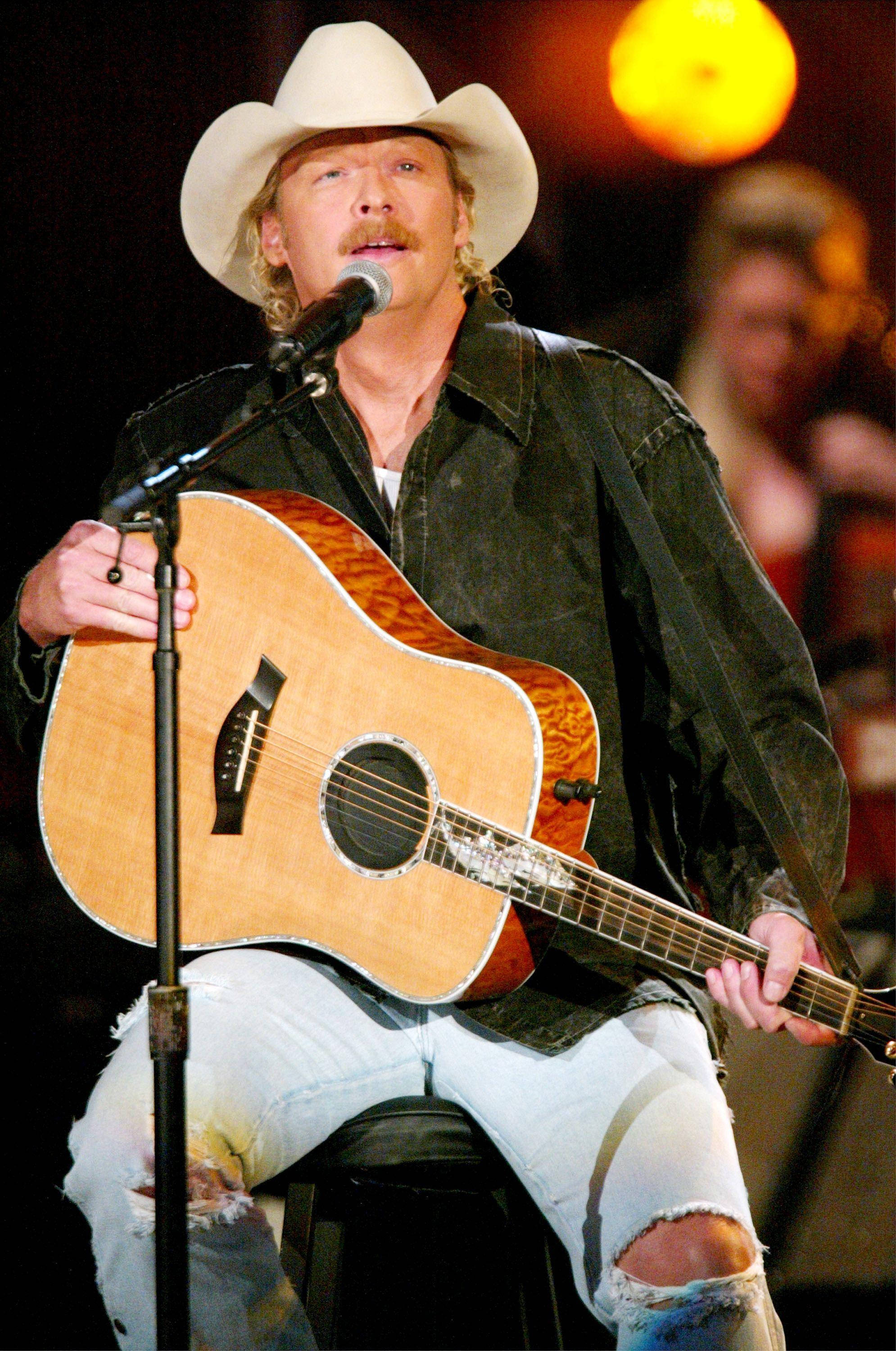Alan Jackson 桌布 壁紙 — 一位鄉村歌手戴著白色牛仔帽和破洞牛仔褲，在溫暖的舞台燈光下彈奏原聲結他。