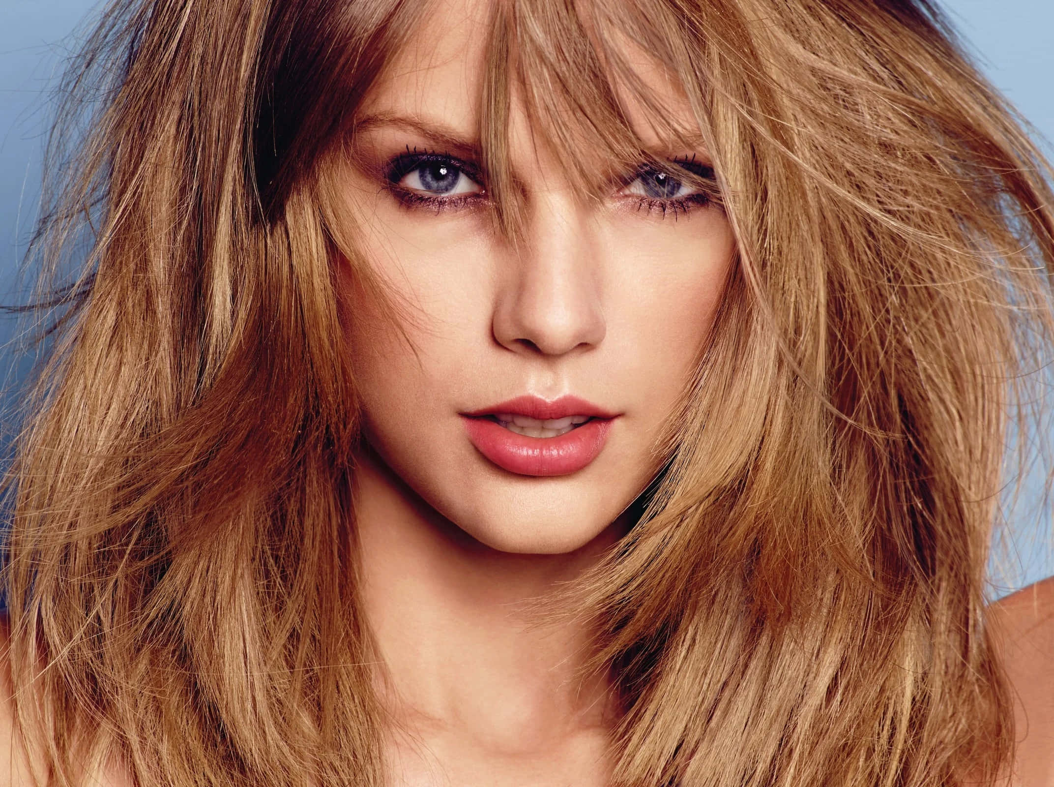 Taylor Swift 桌布 壁紙 — 一位金髮凌亂、藍眼深邃的女性特寫肖像，背景是柔和的藍色。