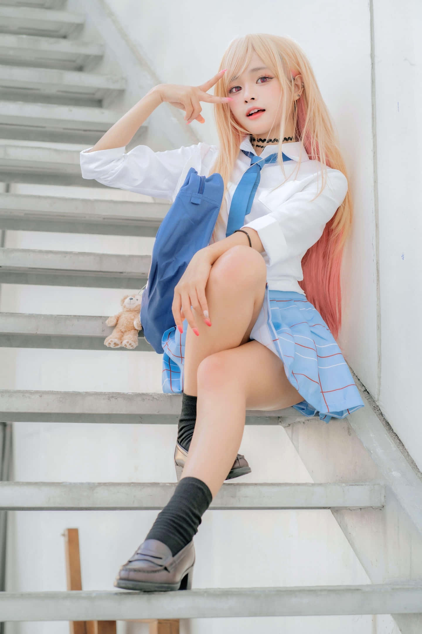Cosplay Anime Kawaii 桌布 壁紙 — 一位金髮動漫女孩穿著藍色校服坐在混凝土樓梯上，旁邊有一個毛絨玩具，比出和平手勢。