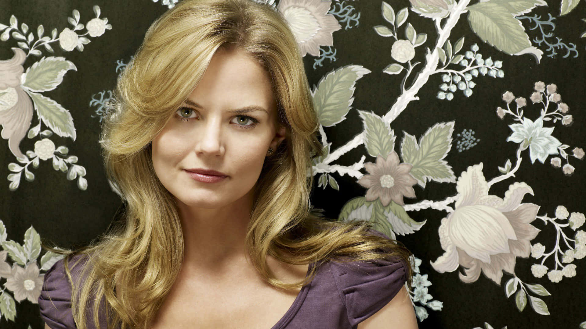 jennifer morrison 桌布 壁紙 — 一位金髮女子帶著柔和波浪，平靜地凝視著深色花卉壁紙，上面有柔和的粉彩花朵。