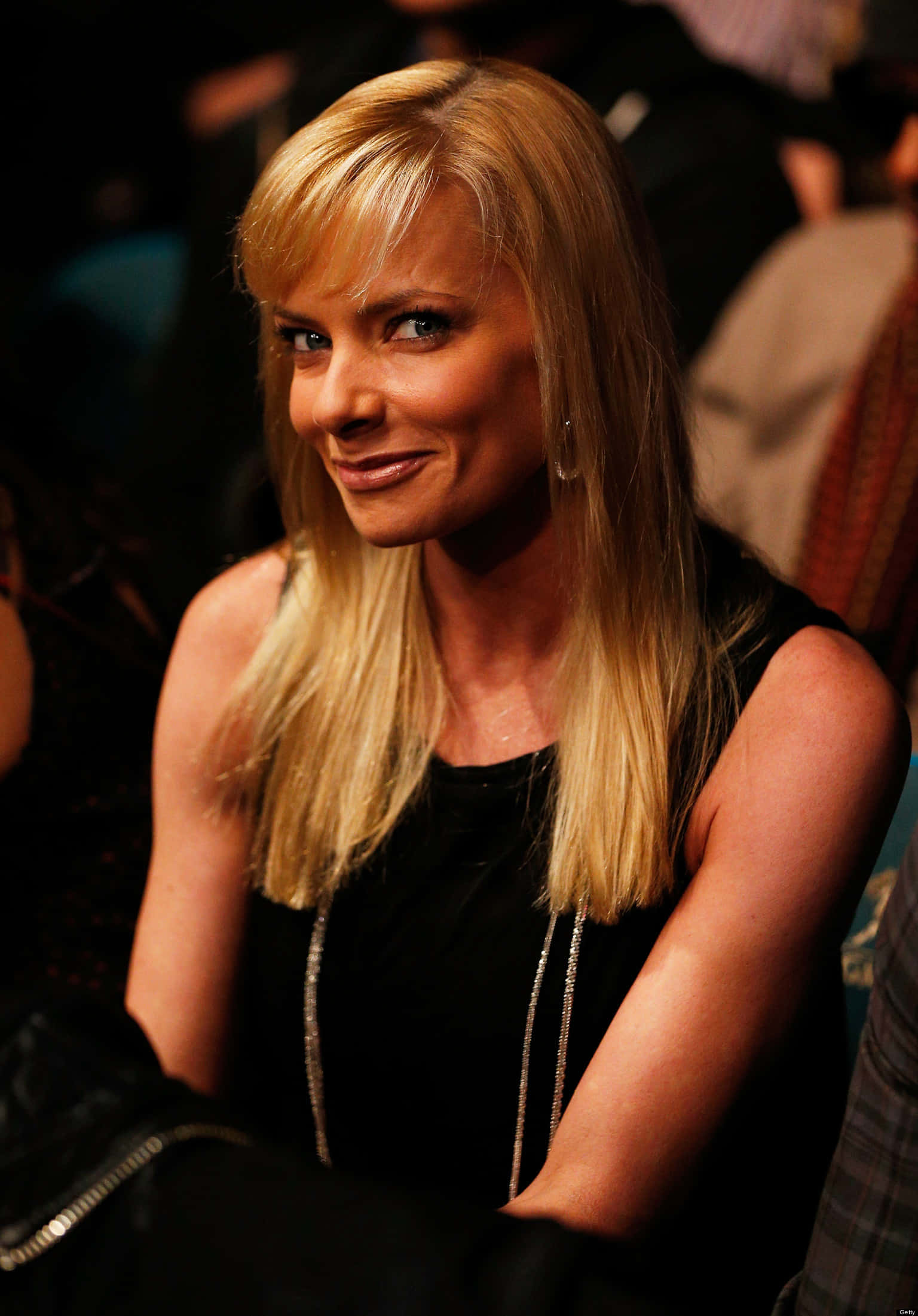Jaime Pressly 桌布 壁紙 — 一位金髮女子帶著溫暖的笑容，在昏暗的環境燈光下穿著黑色上衣和銀色項鍊。