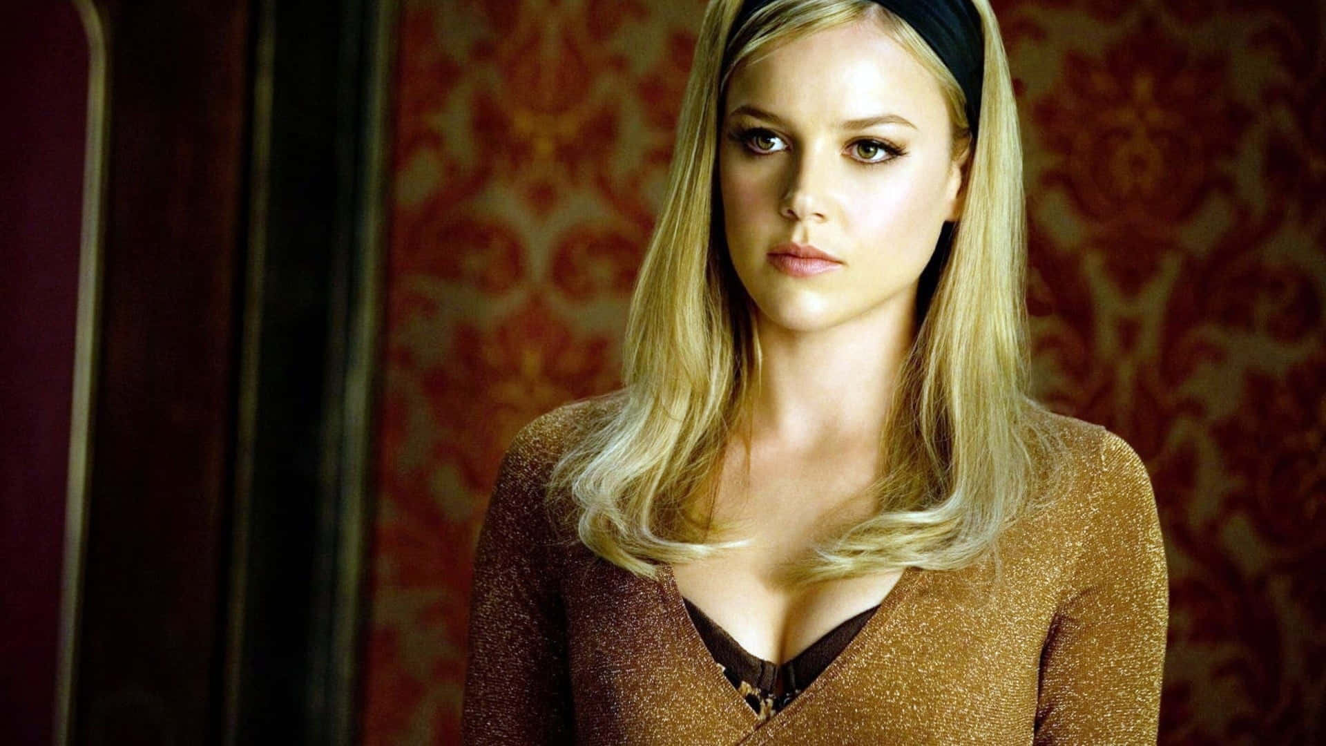 Abbie Cornish 桌布 壁紙 — 一位金髮女子戴著黑色頭帶，對著華麗的紅色錦緞牆紙背景凝視。