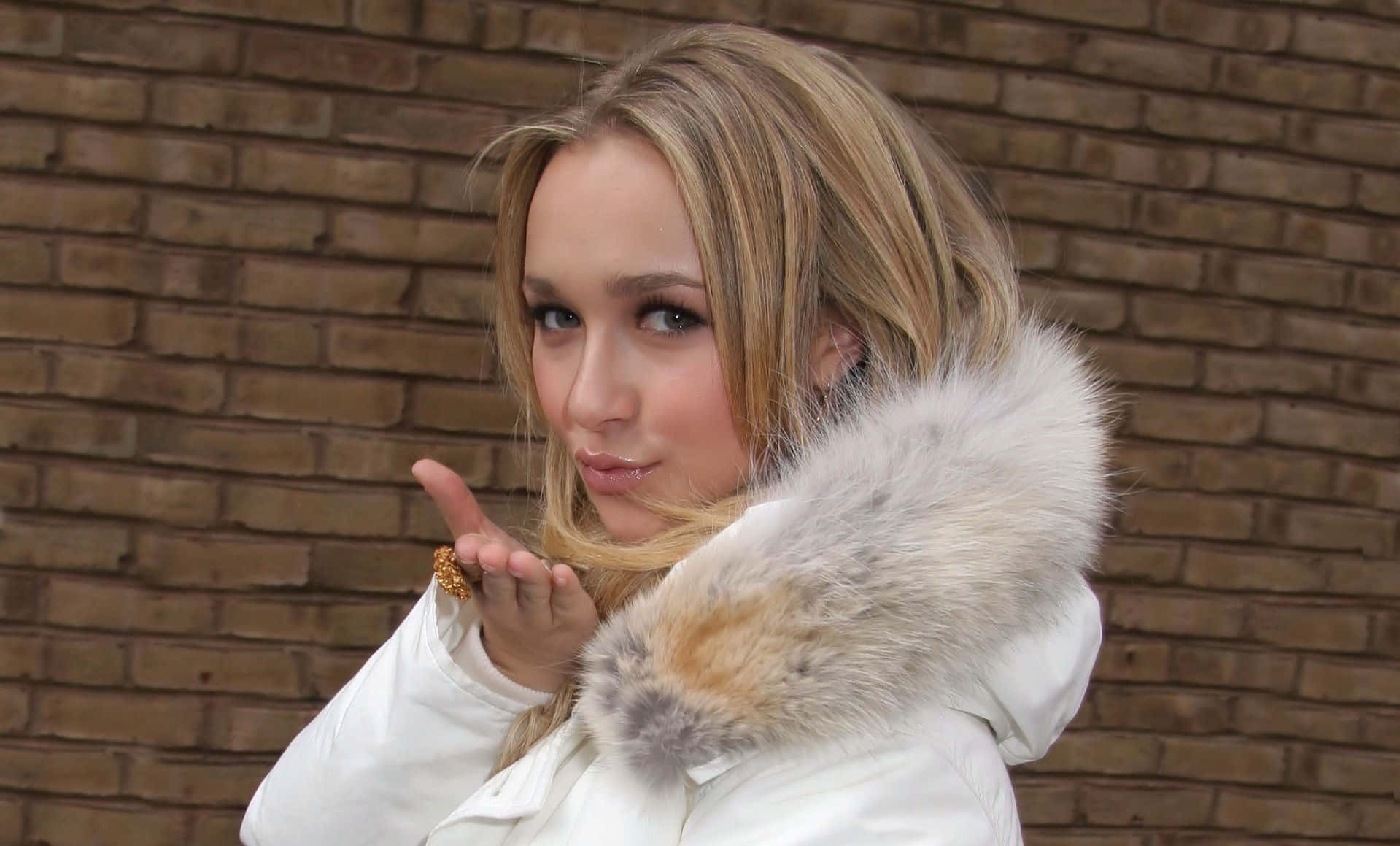 hayden panettiere 桌布 壁紙 — 一位金髮女子穿著白色毛領外套，在磚牆背景下飛吻。