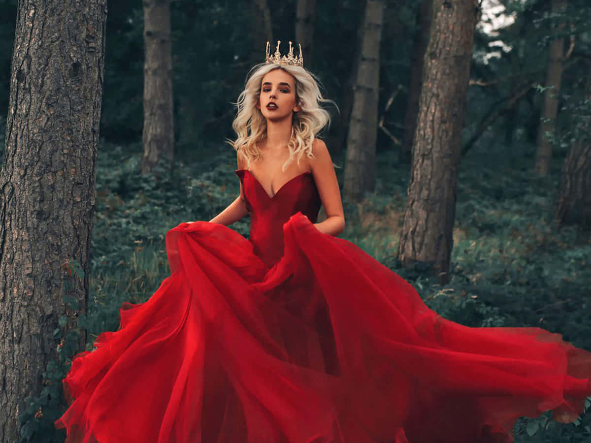 Red Wedding 桌布 壁紙 — 一位金髮女子身穿飄逸的紅色長袍，頭戴金色皇冠，以戲劇性的姿態站在高大的森林樹木之間。