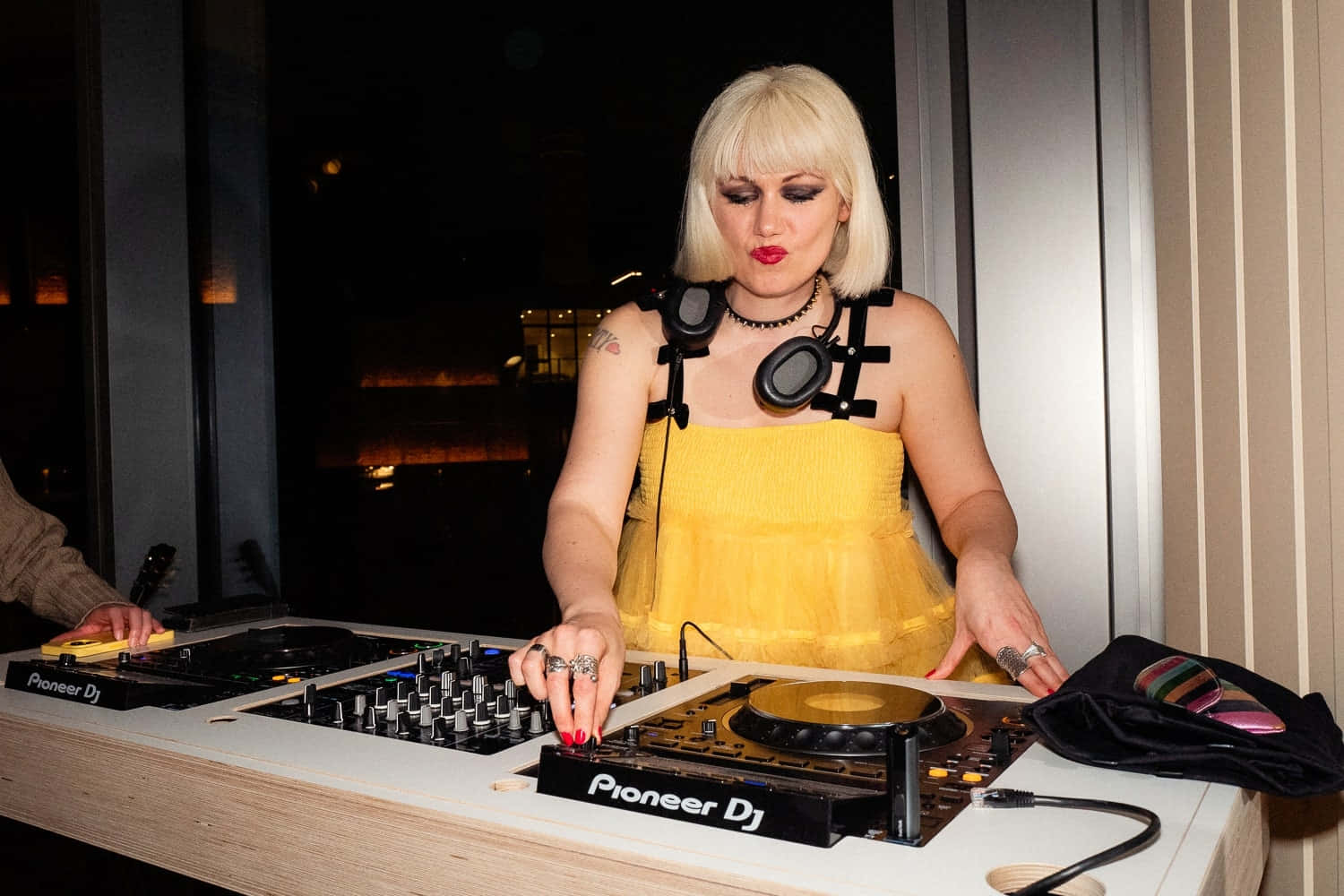 DJ 桌布 壁紙 — 一位金髮女子身穿黃色連衣裙，在溫暖的室內燈光下用Pioneer DJ混音台混音。