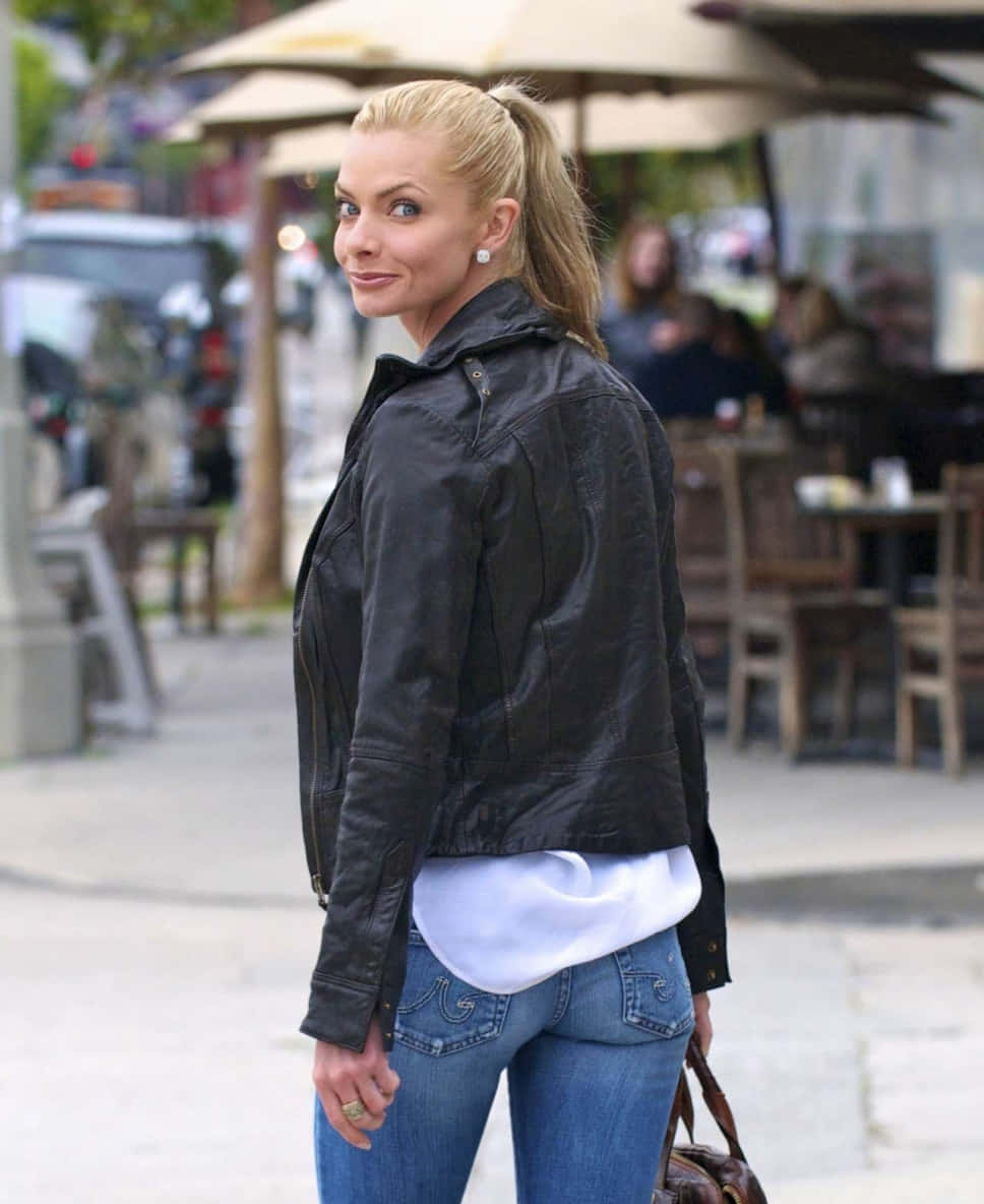 Jaime Pressly 桌布 壁紙 — 一位金髮女子身穿黑色皮褸和牛仔褲，在繁忙的城市行人路上轉身向鏡頭微笑。