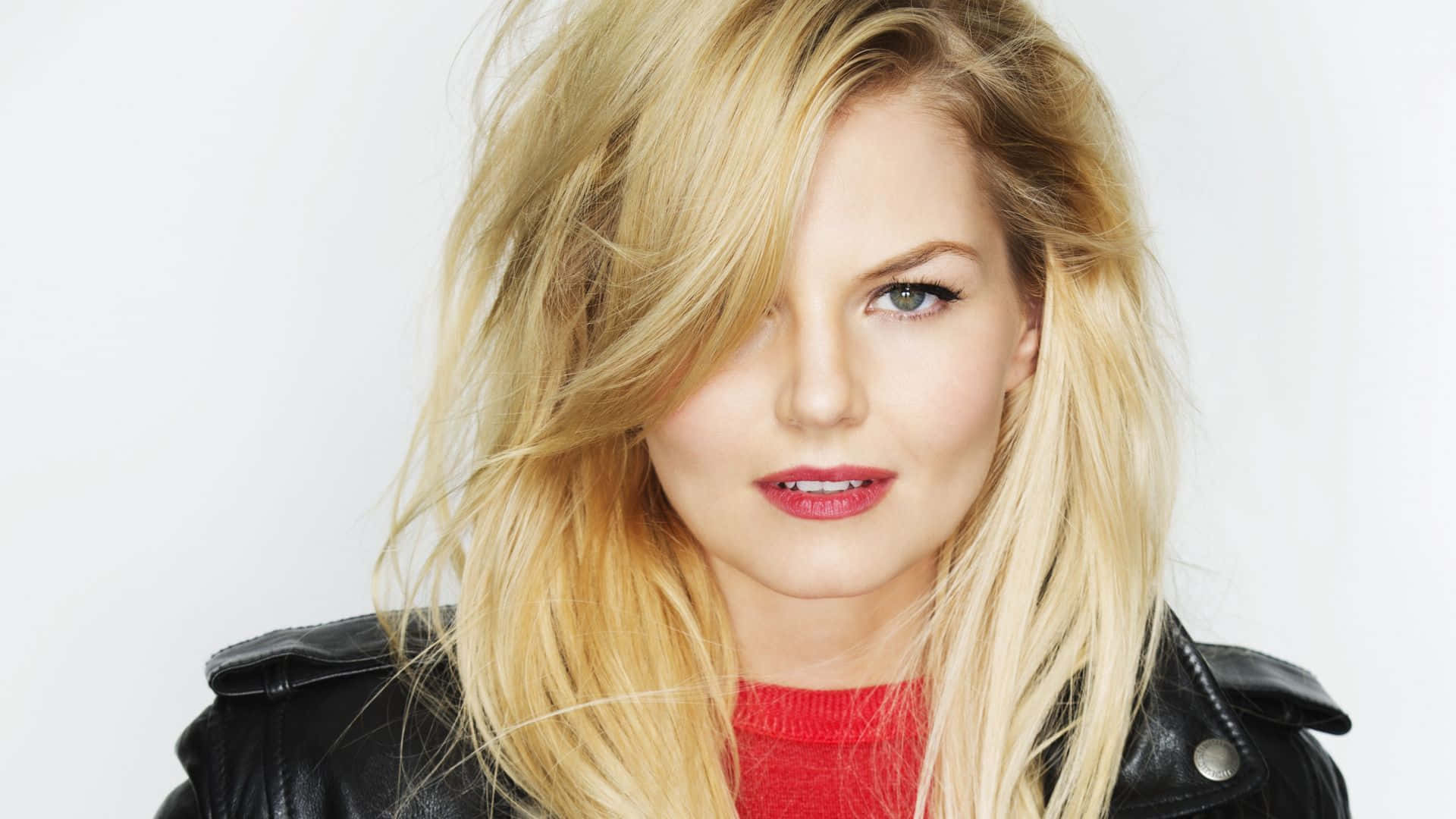 jennifer morrison 桌布 壁紙 — 一位金髮女子頭髮被風吹起，在純白背景前穿著黑色皮褸內搭紅色毛衣。