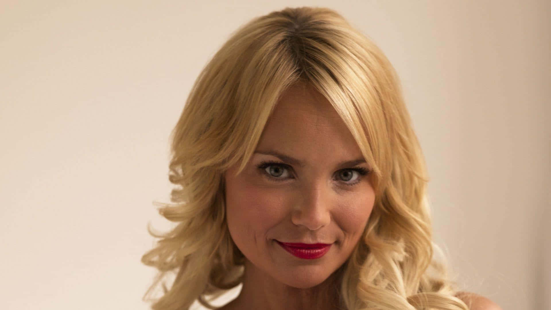 kristin chenoweth 桌布 壁紙 — 一位金髮女性嘅特寫肖像，佢有鮮紅色嘅嘴唇，喺純米色背景前輕輕微笑。