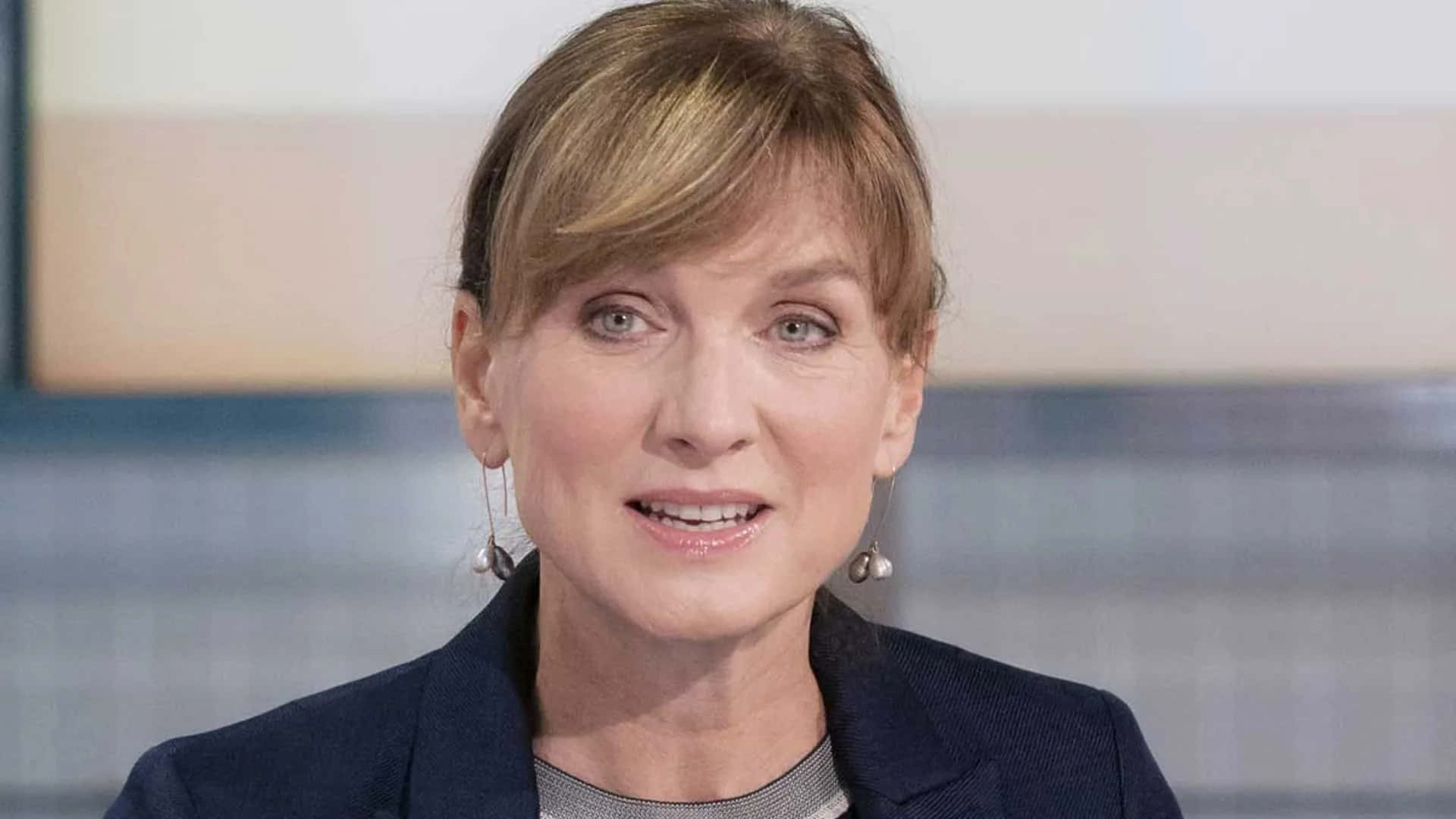 Fiona Bruce 桌布 壁紙 — 一位金髮女性嘅近距離肖像，穿著深色西裝外套同珍珠耳環，背景模糊。