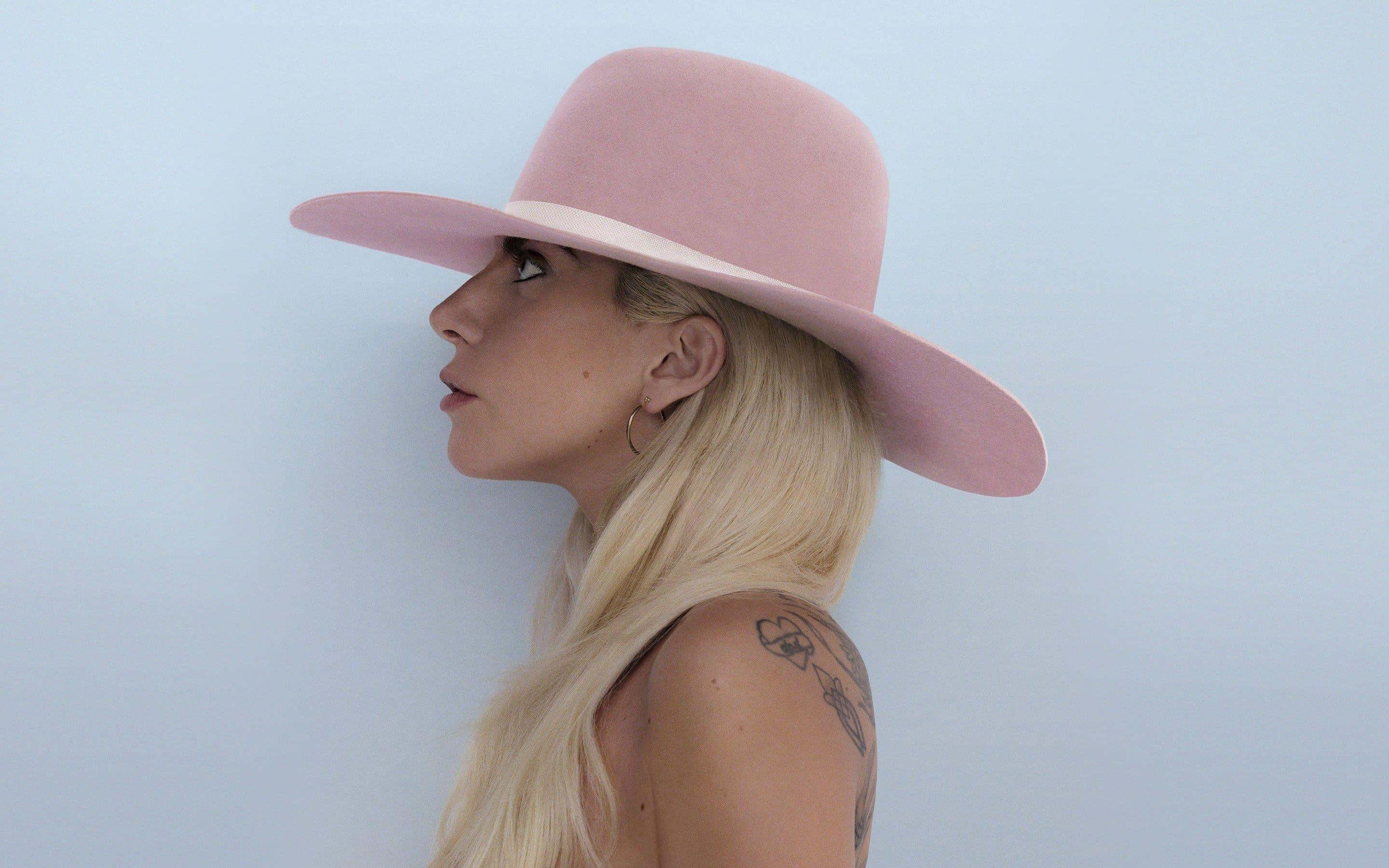 Lady Gaga 桌布 壁紙 — 一位金髮女性戴著一頂寬邊粉紅色帽子，背景是柔和的藍色。