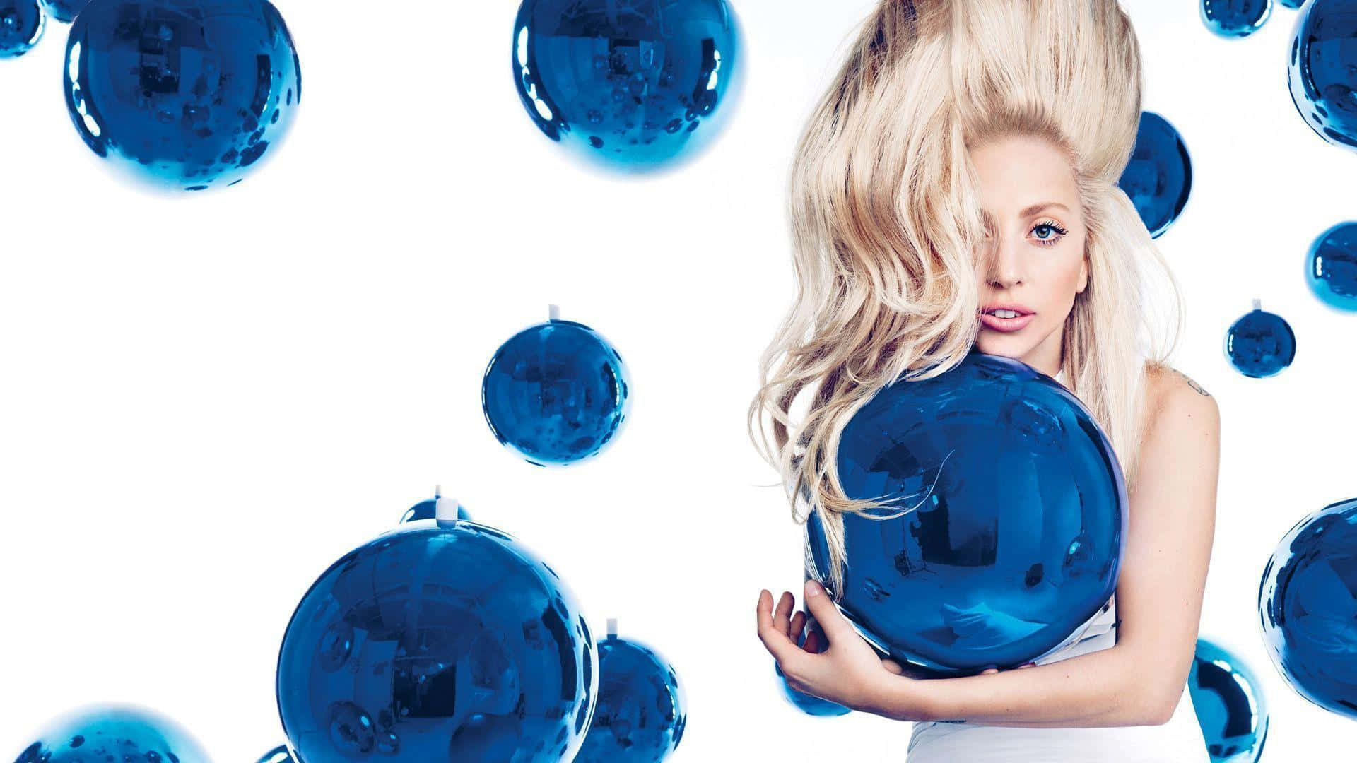 Lady Gaga 桌布 壁紙 — 一位金髮女性手持一個大型藍色鏡面球，周圍漂浮著迪斯科球，背景為純白色。