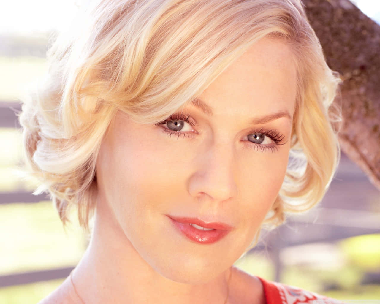 Jennie Garth 桌布 壁紙 — 一位金髮女性的特寫肖像，擁有柔軟的捲髮和溫柔的微笑，沐浴在溫暖的陽光中。