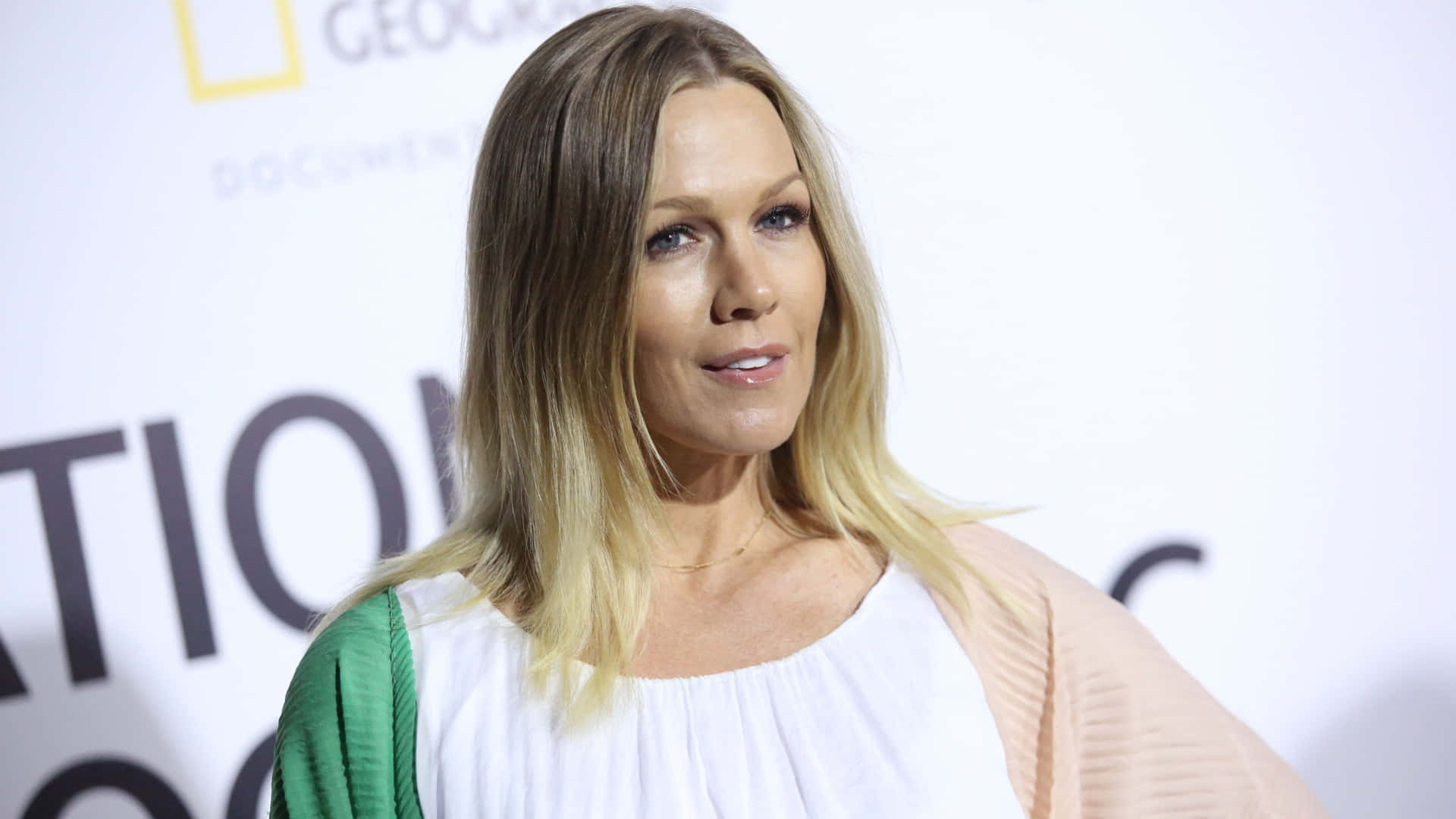 Jennie Garth 桌布 壁紙 — 一位金髮女性穿著白色上衣和綠色袖子，站在國家地理活動中，背景模糊。
