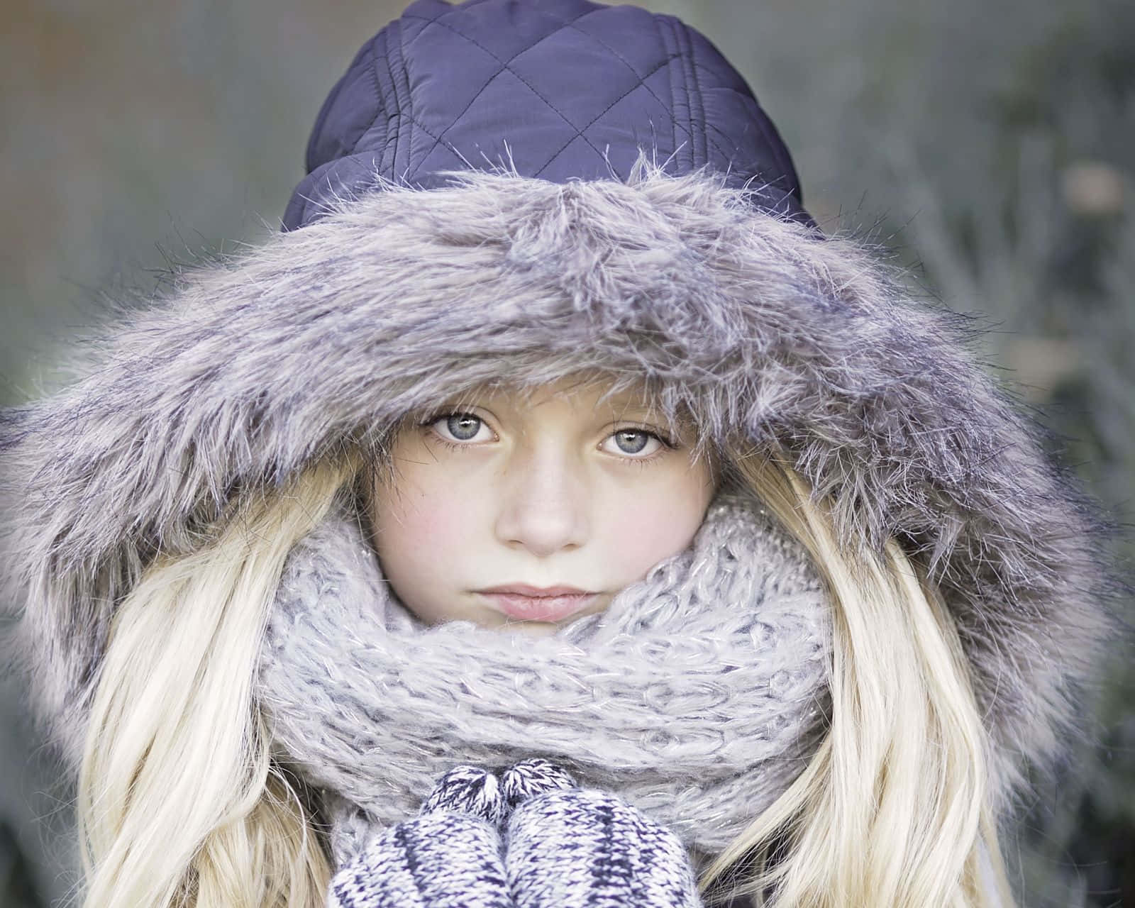 Winter Fashion 桌布 壁紙 — 一位金髮小女孩戴著毛絨內襯的連帽和厚圍巾，背景是模糊的冬日景色。