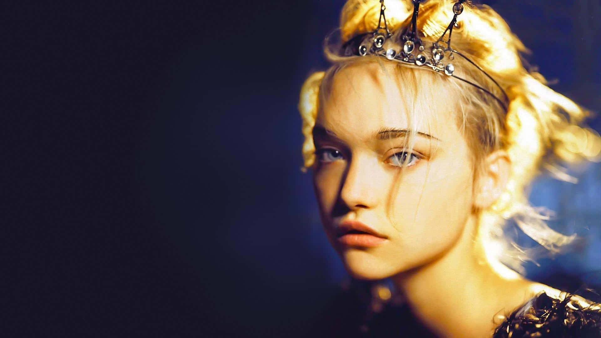 Gemma Ward 桌布 壁紙 — 一位金髮年輕女子戴著鑲有寶石的王冠，在深藍色背景和金色燈光下專注地凝視。