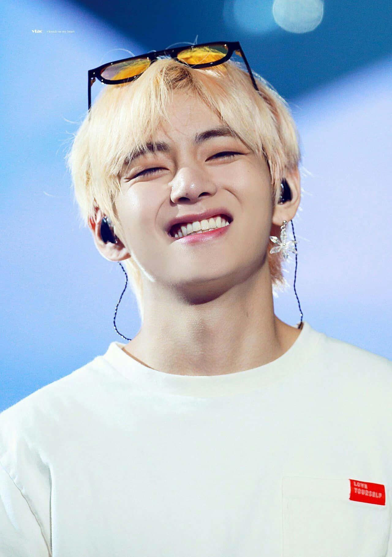 Taehyung Cute 桌布 壁紙 — 一位金髮年輕男子，頭頂上架著太陽眼鏡，戴著耳機和白色T恤，滿臉喜悅。