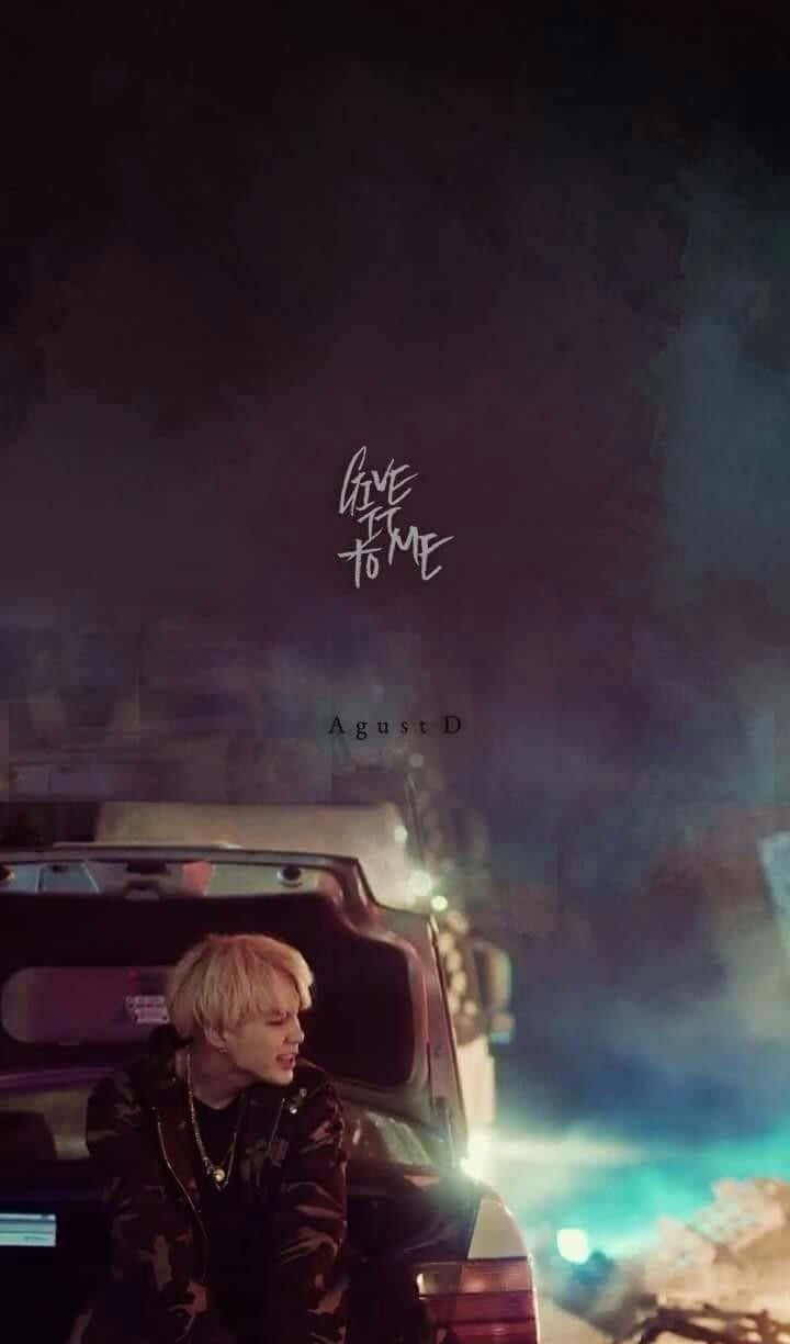 Agust D 桌布 壁紙 — 一位金髮年輕男子在夜晚坐在車旁，周圍有發光的藍色燈光和煙霧繚繞。