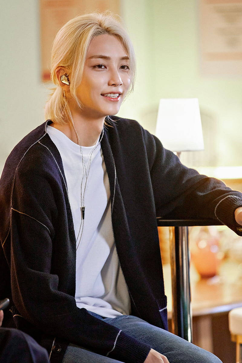 Yoon Jeonghan Open Mic 壁紙 — 一位金髮年輕男子在室內戴著耳塞和黑色開襟衫微笑。