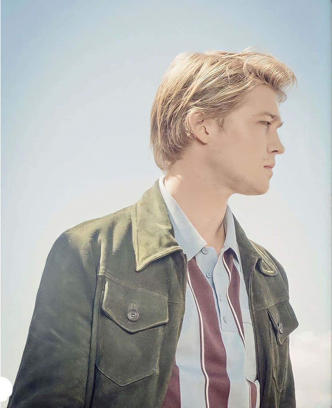 Joe Alwyn 桌布 壁紙 — 一位金髮年輕男子穿著綠色外套和條紋襯衫，背景是柔和的藍天。