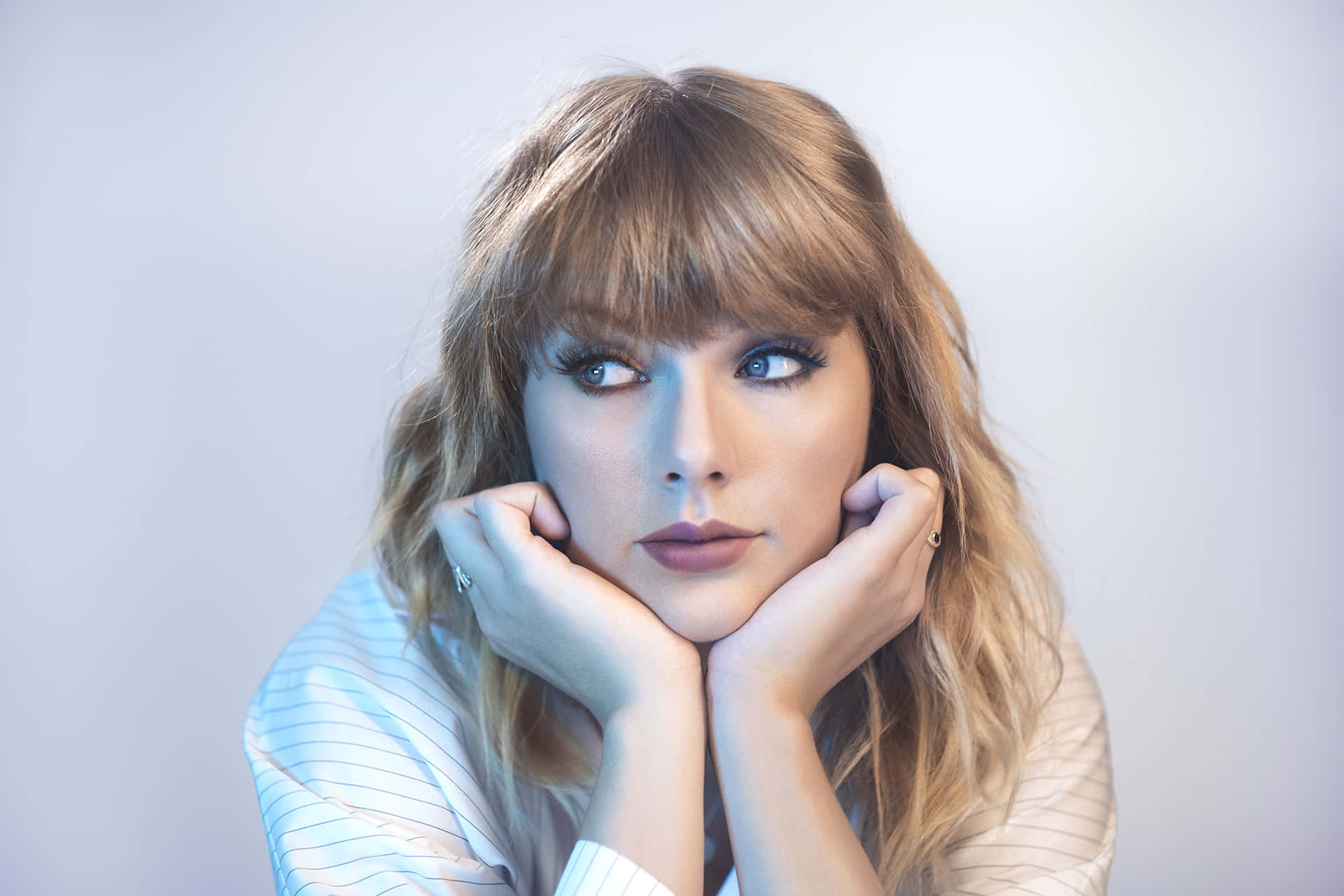 Taylor Swift 桌布 壁紙 — 一位金髮有瀏海的女性，雙手托腮，背景是純淺灰色。