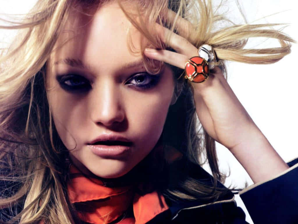 Gemma Ward 桌布 壁紙 — 一位金髮模特兒帶着煙燻眼妝和搶眼的橙色戒指，在純白背景前凝視鏡頭。