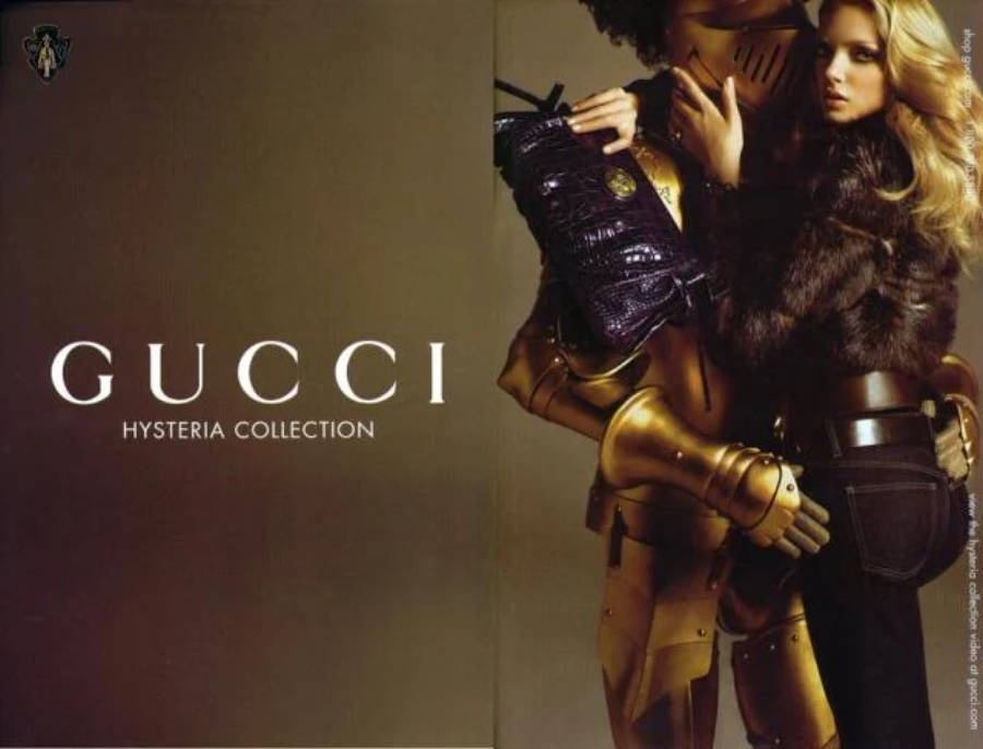 Gucci 桌布 壁紙 — 一位金髮模特兒穿著皮草和牛仔褲，與一個金色盔甲人物拿著紫色鱷魚皮手袋，在柔和的棕色背景前擺姿勢。
