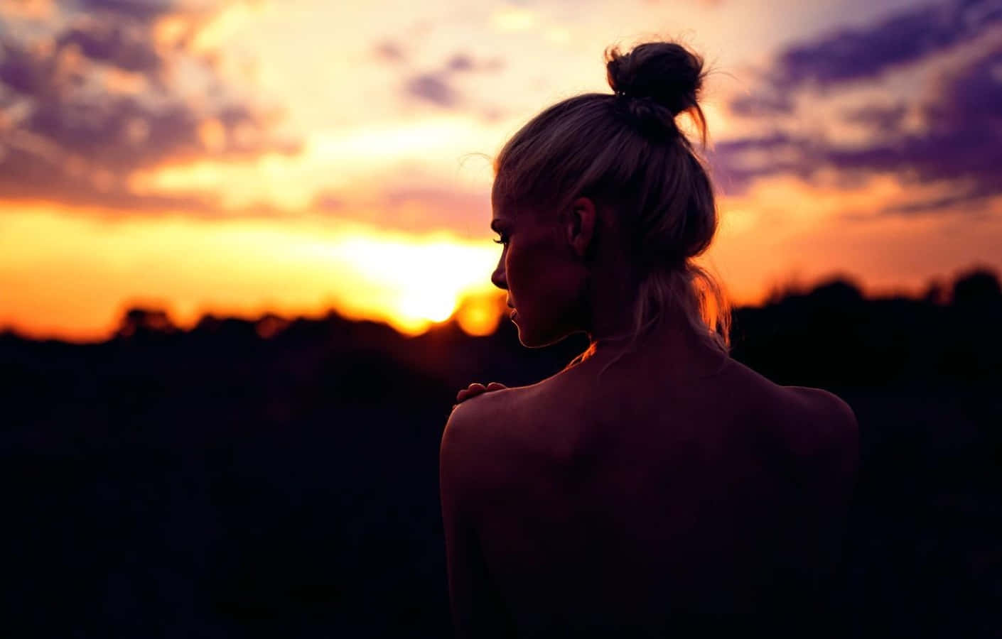 Sunset Silhouette 桌布 壁紙 — 一位金髮盤成髮髻的女性凝視著黑暗地平線上方充滿活力的橙色和紫色日落。