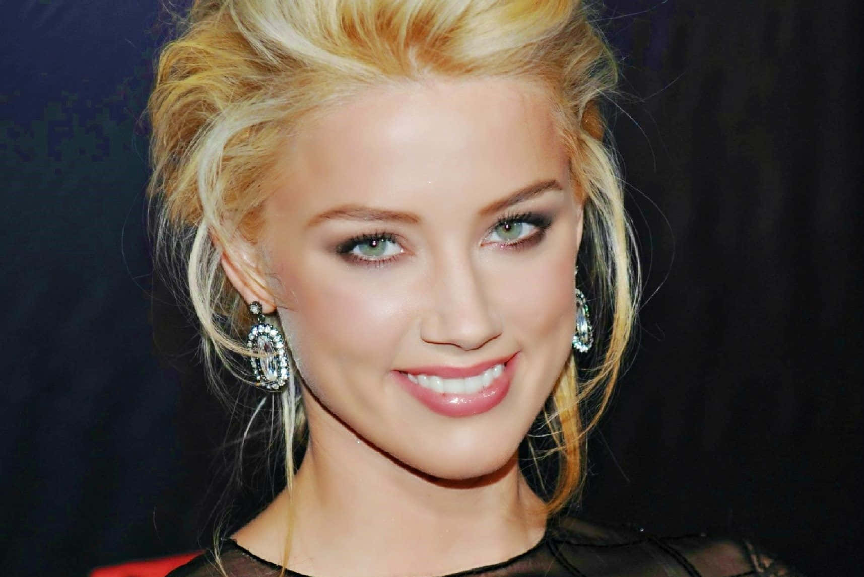 Amber Heard 桌布 壁紙 — 一位金髮碧眼女子在深色背景下溫暖微笑的特寫肖像。