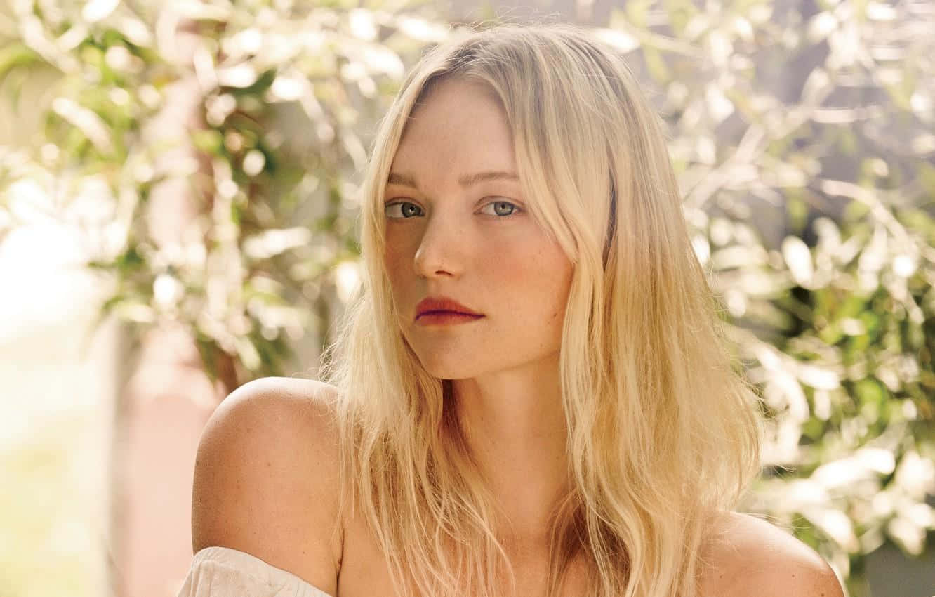 Gemma Ward 桌布 壁紙 — 一位金髮碧眼溫柔的女性，在陽光普照、模糊的綠色樹葉背景下若有所思地凝視著。