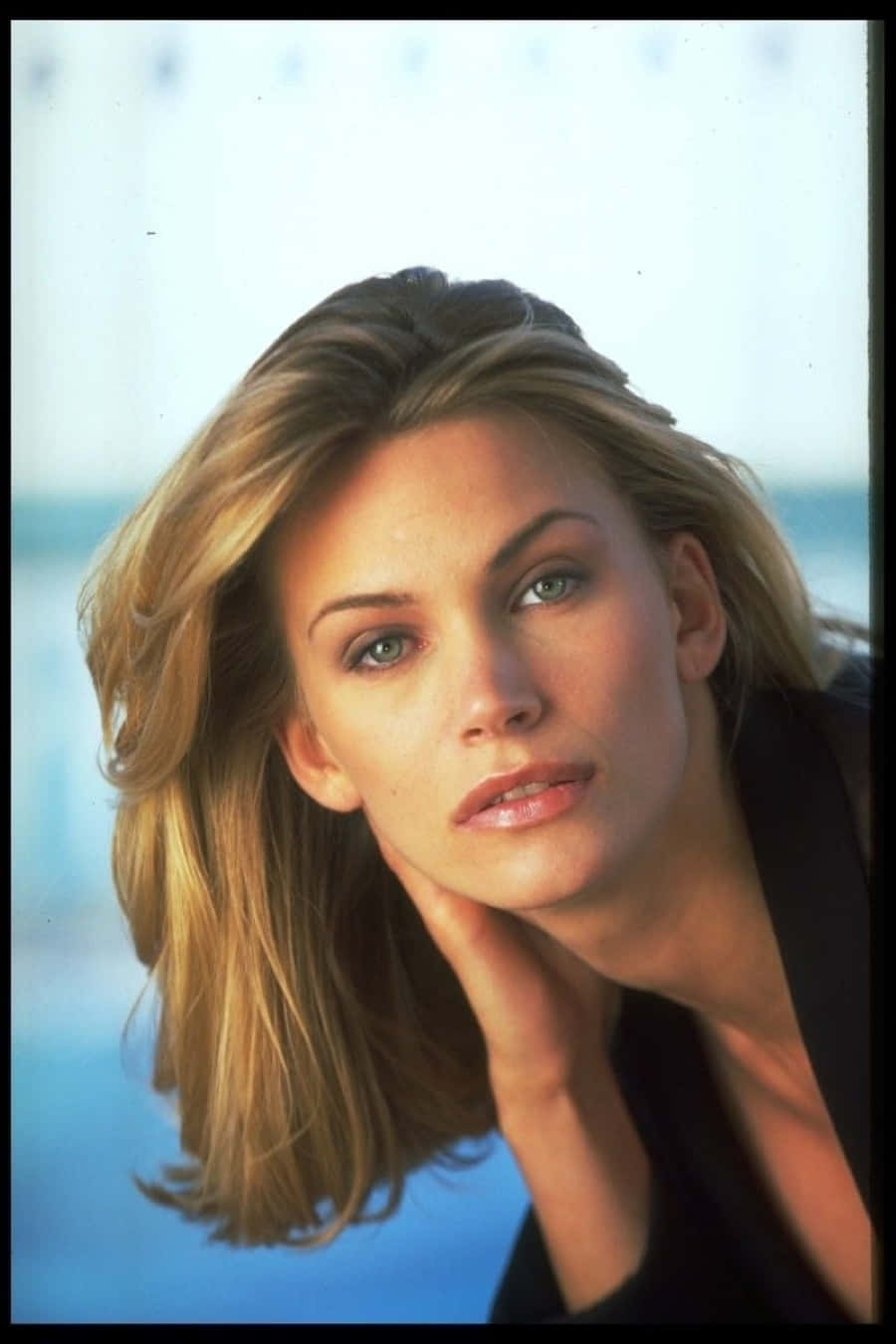 Natasha Henstridge 桌布 壁紙 — 一位金髮碧眼的女性，在模糊的藍色背景前，托腮沉思。