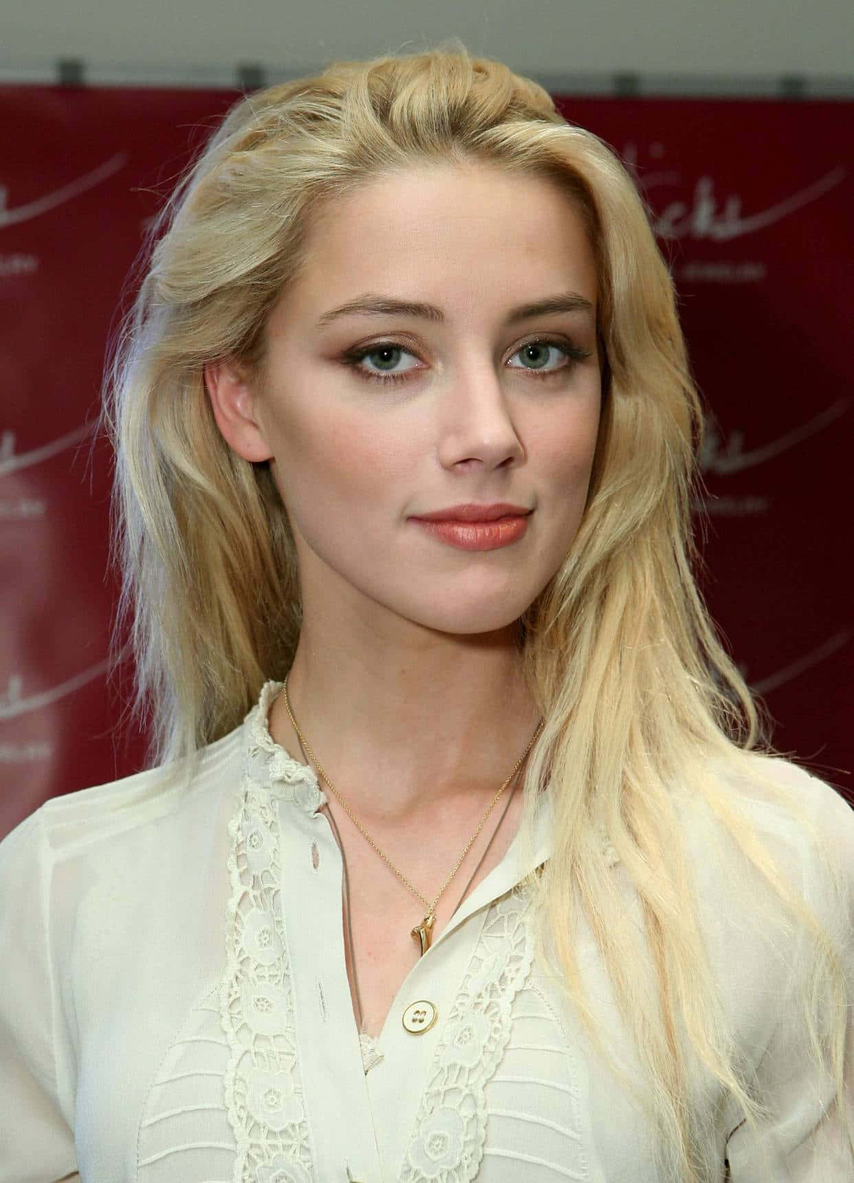 Amber Heard 桌布 壁紙 — 一位金髮碧眼的白人女性身穿白色蕾絲襯衫，在紅色品牌背景前的特寫肖像。