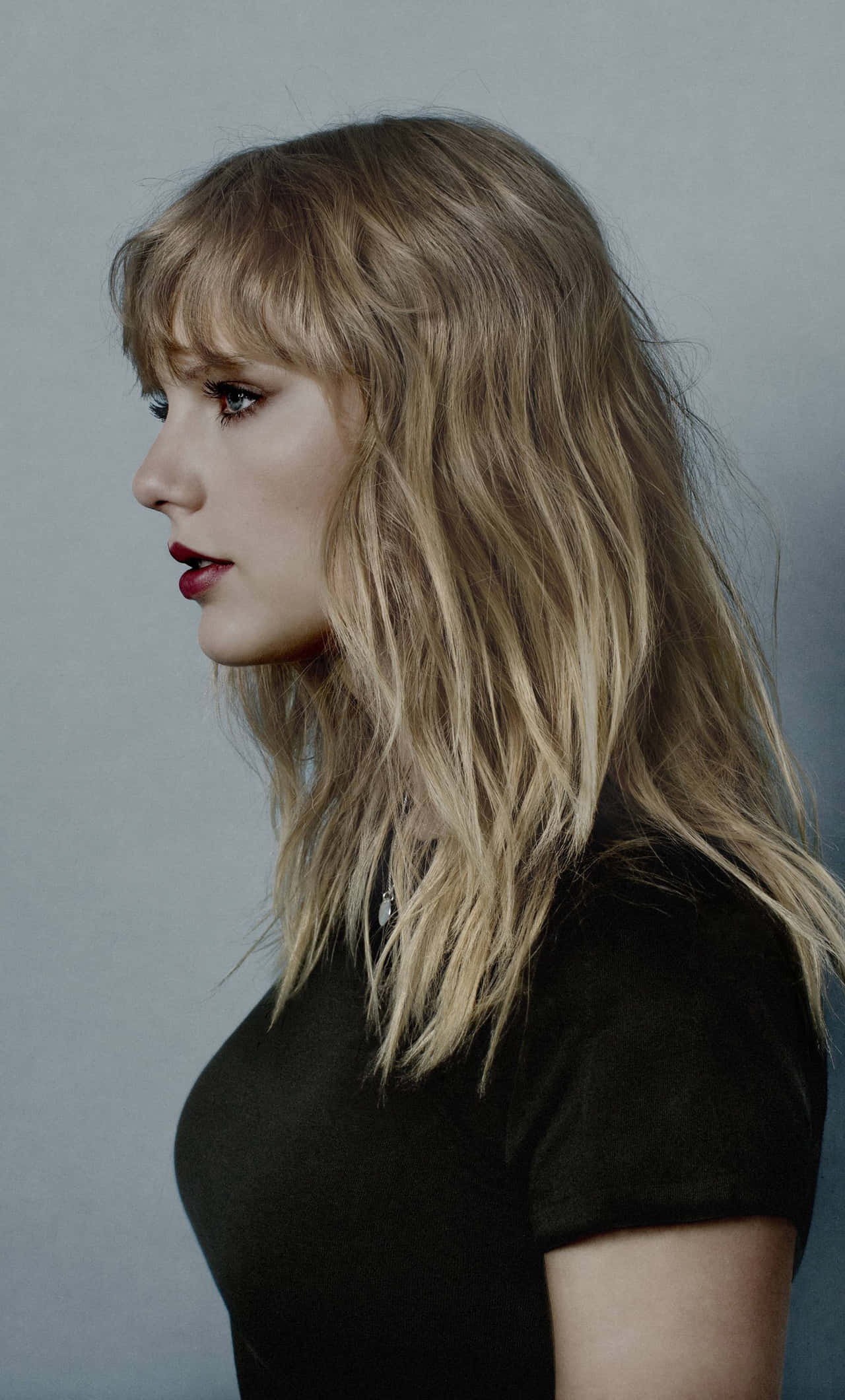 Taylor Swift 桌布 壁紙 — 一位金髮紅唇的女性在柔和的灰色背景下若有所思地凝視。