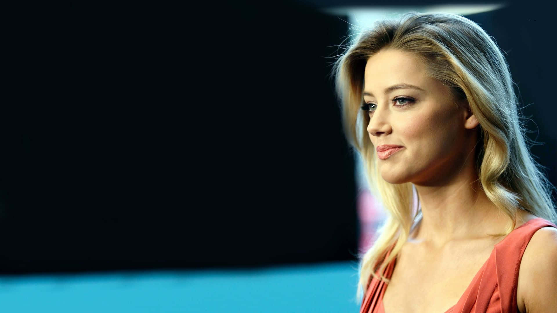 Amber Heard 桌布 壁紙 — 一位金髮紅裙的女性在藍色地板的深色背景下若有所思地凝視。