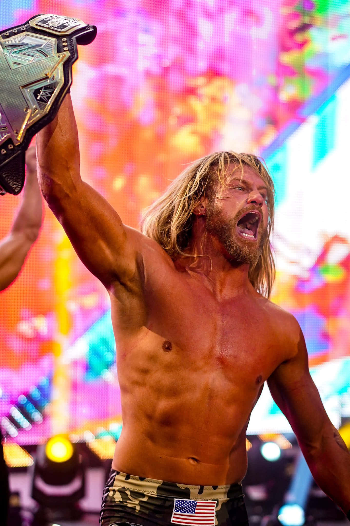 Dolph Ziggler United States Champion 壁紙 — 一位金髮肌肉發達的摔角手在色彩繽紛的LED背景下勝利地高舉冠軍腰帶。