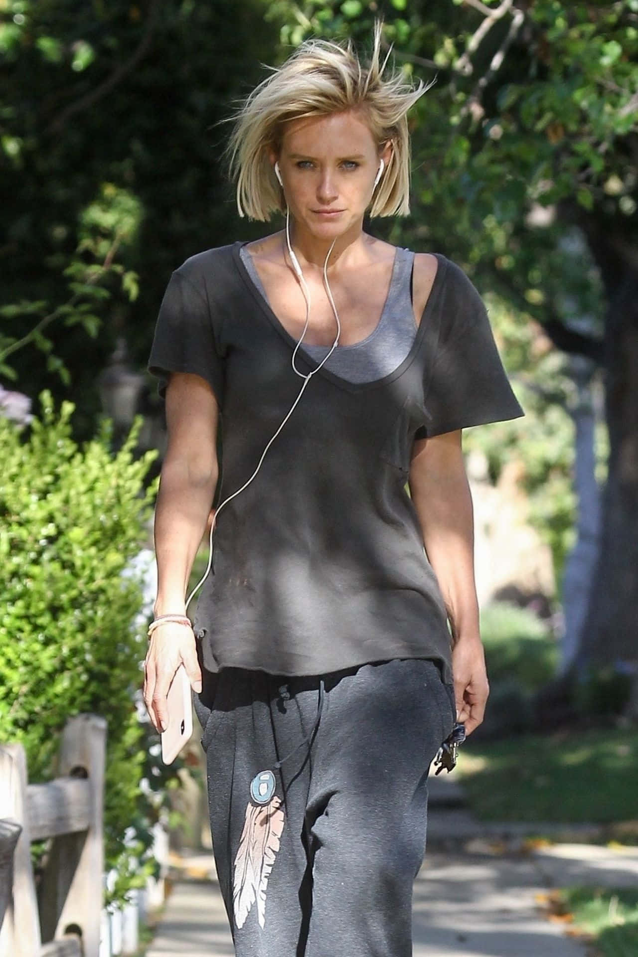 Nicky Whelan 桌布 壁紙 — 一位金髮蓬鬆的女性在陽光明媚的日子裡穿著灰色運動服和白色耳塞在戶外行走。