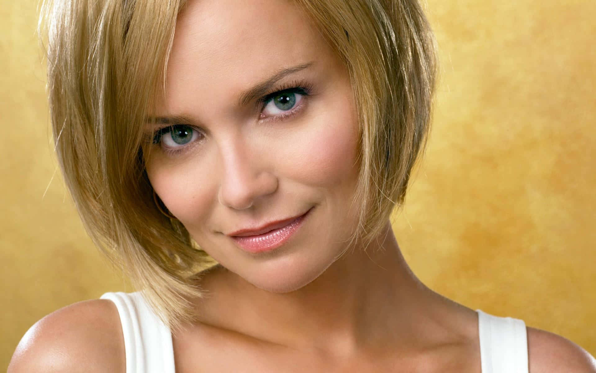 kristin chenoweth 桌布 壁紙 — 一位金髮藍眼女士在溫暖金色背景前微笑的特寫肖像。