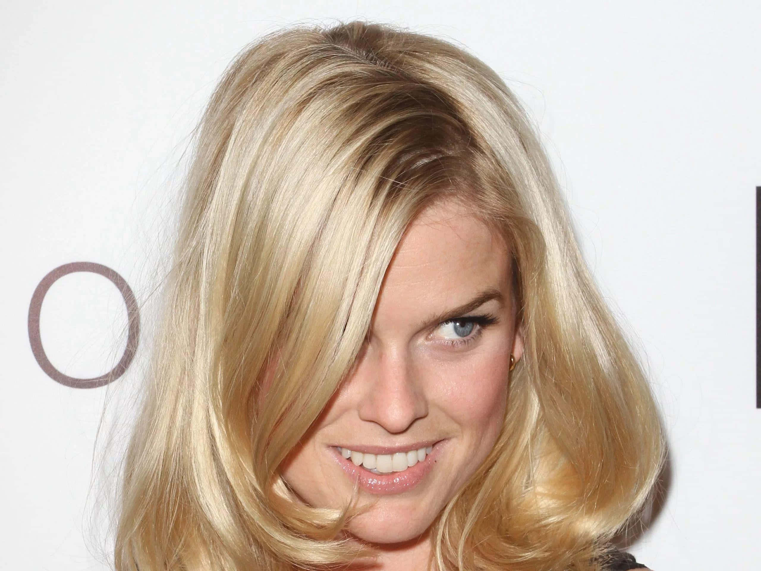 alice eve 桌布 壁紙 — 一位金髮藍眼女子的特寫，她頑皮地微笑，頭髮部分遮蓋了她的臉龐。