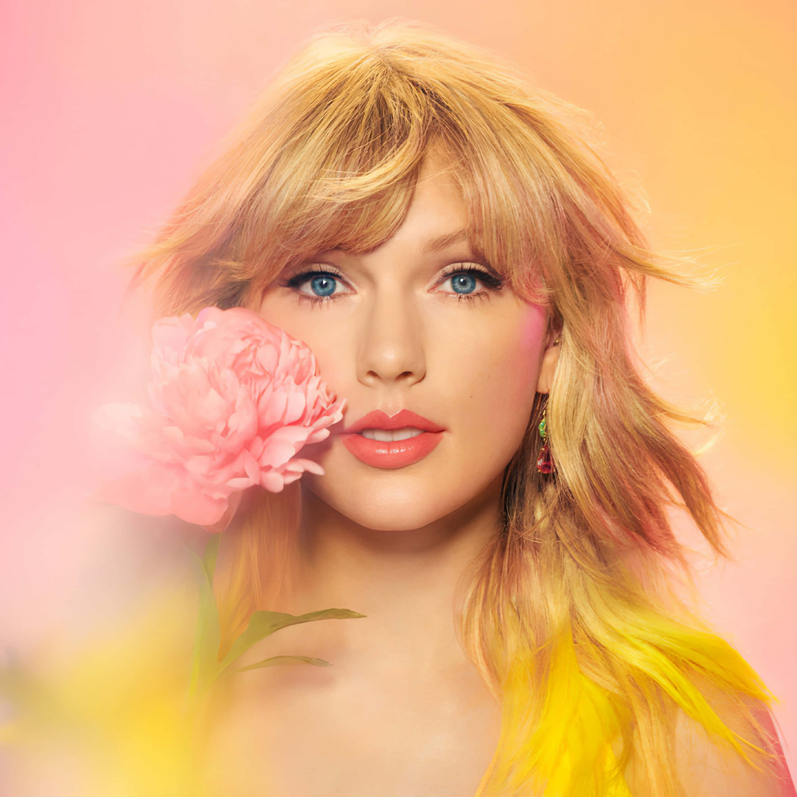 Taylor Swift 桌布 壁紙 — 一位金髮藍眼的女人在柔和的粉黃漸變背景前，將一朵粉紅牡丹靠近臉龐。