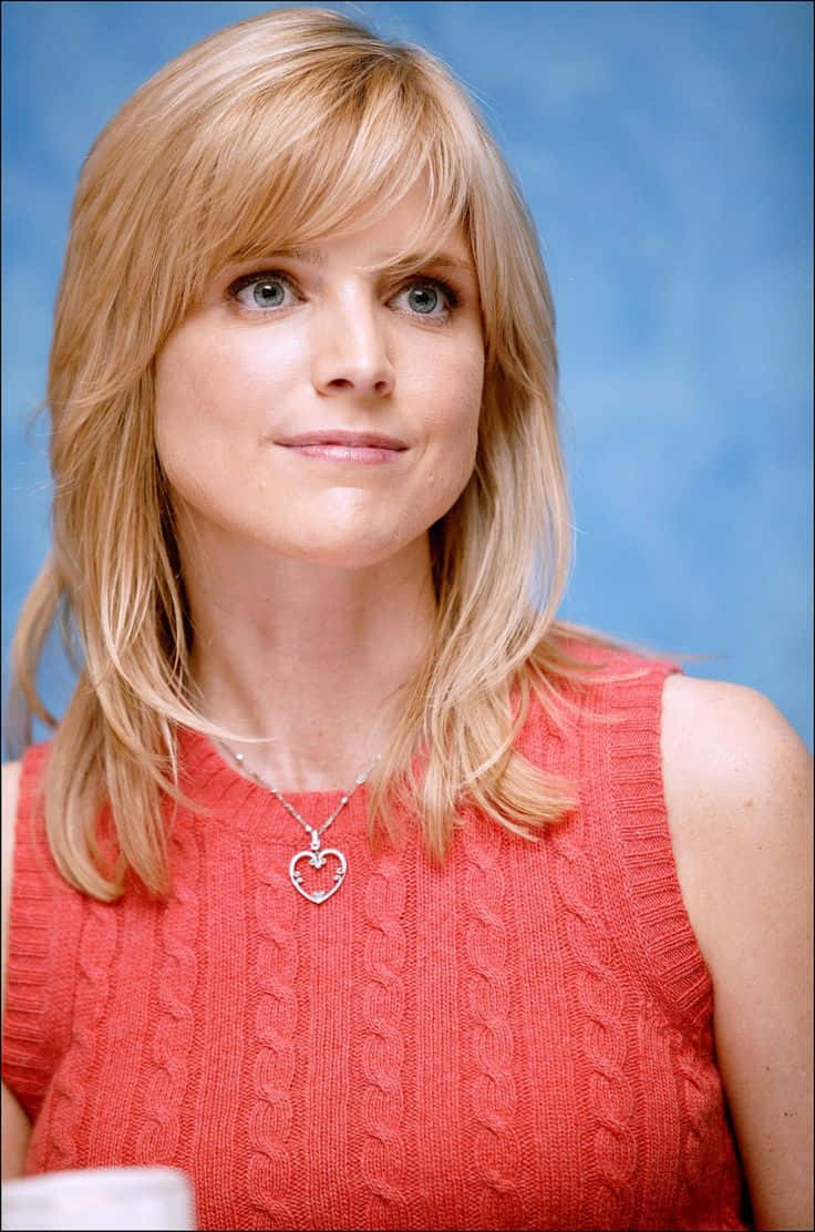Courtney Thorne Smith 桌布 壁紙 — 一位金髮藍眼的女性在藍色背景前穿著紅色麻花針織上衣。