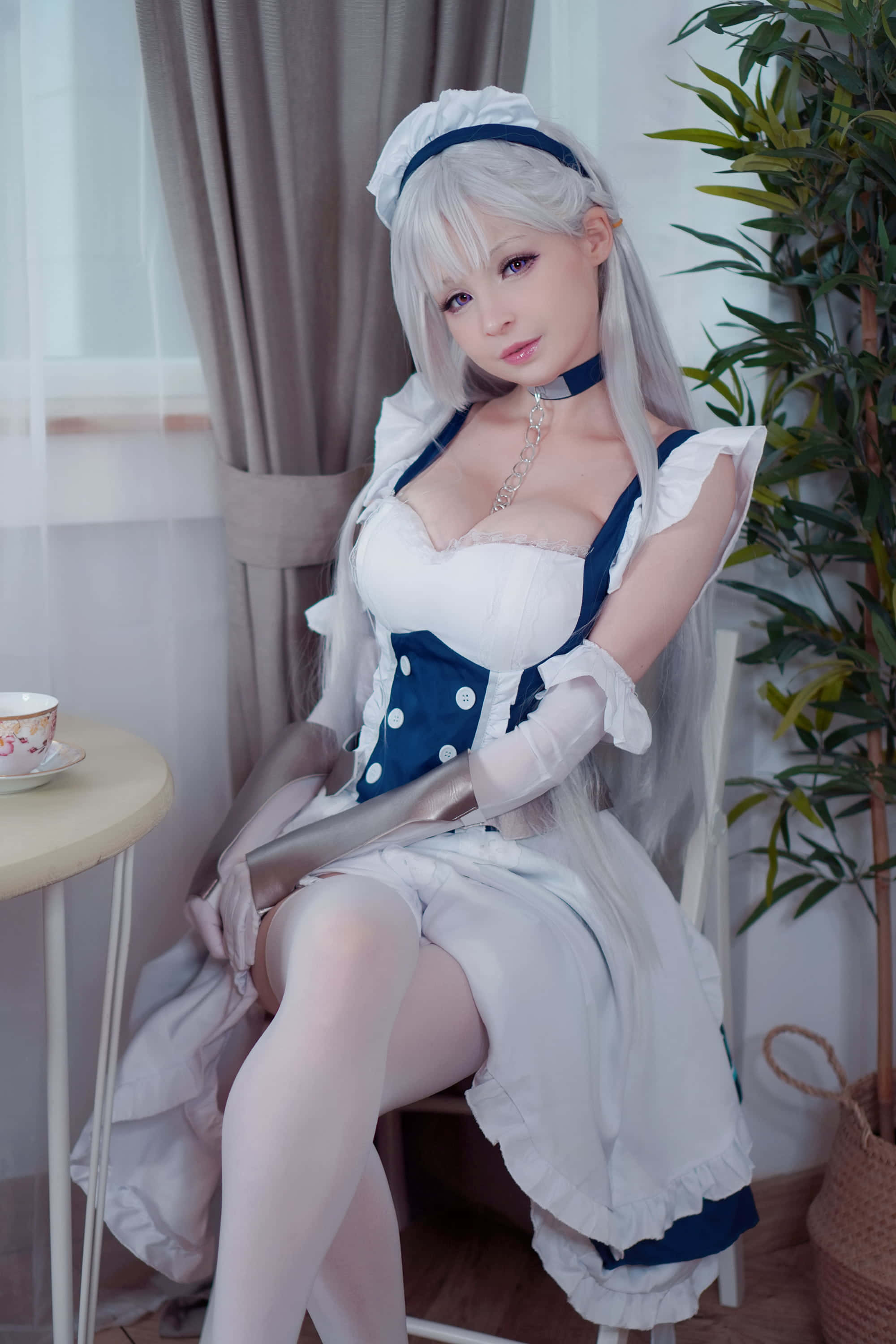 Gaming Cosplay 桌布 壁紙 — 一位銀髮女僕穿著白色和藍色的連衣裙，優雅地坐在窗邊，旁邊有一盆盆栽植物。