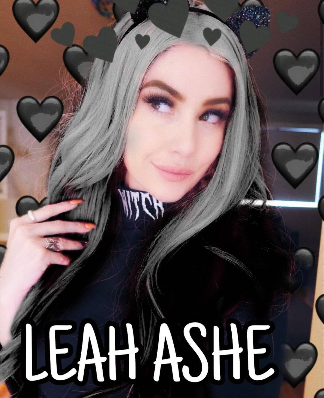 YouTuber Leah Ashe 壁紙 — 一位銀髮貓耳女性微笑著，身穿被黑色心形圖案包圍的女巫高領毛衣。
