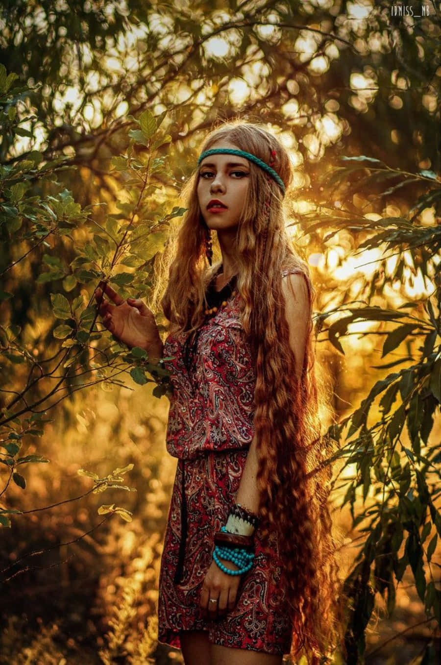 嬉皮士 桌布 壁紙 — 一位長捲髮、穿著波希米亞風格服裝的年輕女性，站在陽光灑落的樹林中，沐浴在黃金時刻的溫暖中。
