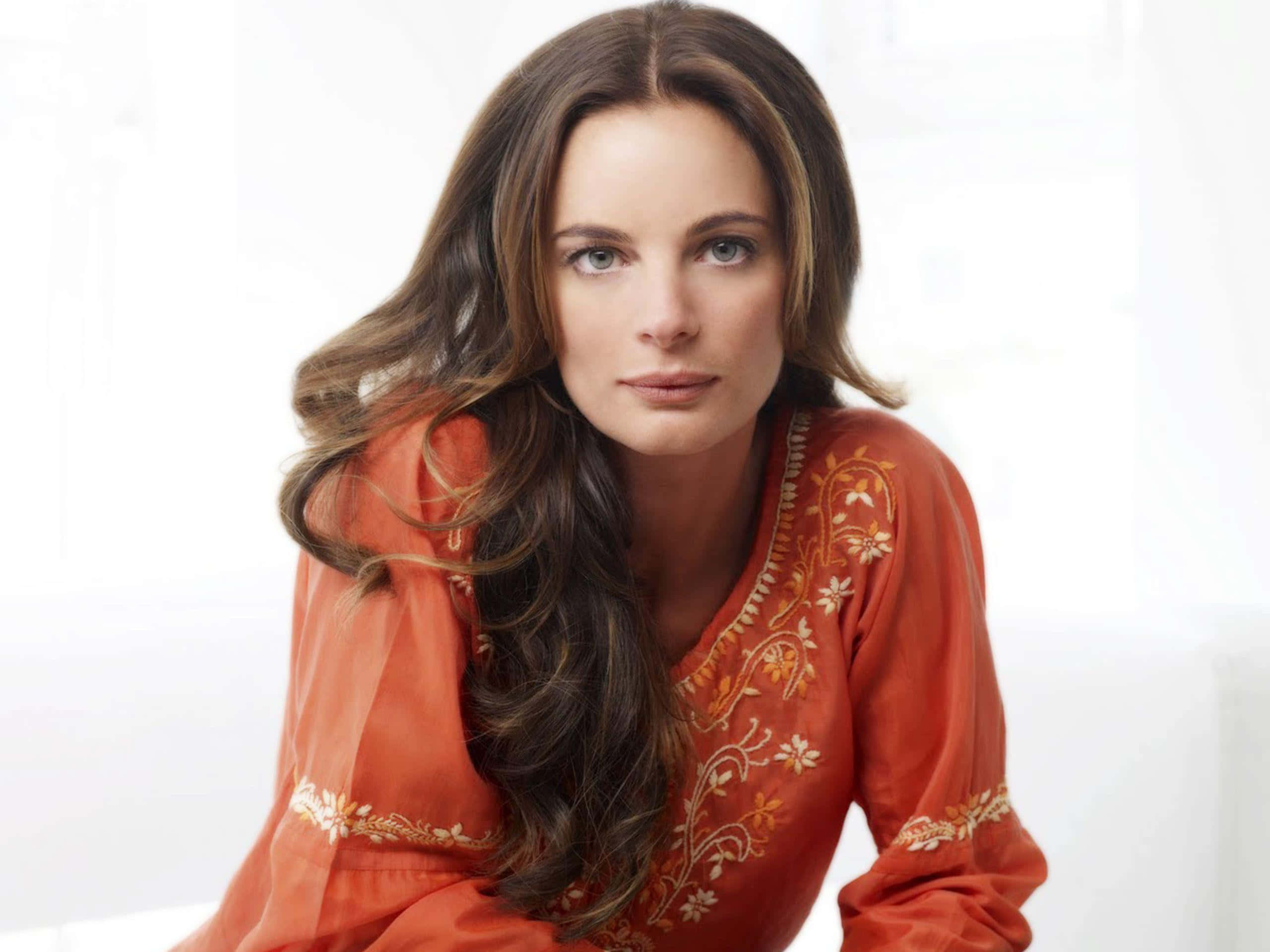 Gabrielle Anwar 桌布 壁紙 — 一位長棕色頭髮的女性，在明亮的白色背景前穿著橙色刺繡上衣。