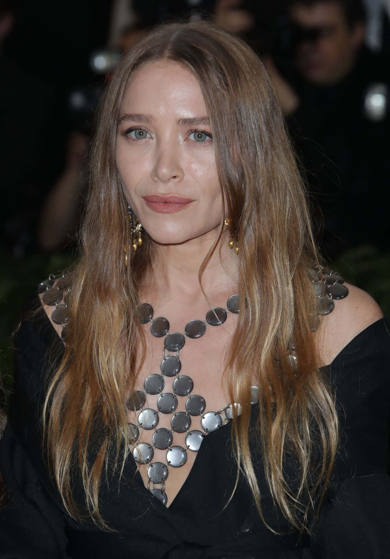 Mary Kate Olsen 桌布 壁紙 — 一位長棕髮女性在華麗活動中佩戴大膽的銀色圓盤項鍊和黑色露肩上衣。