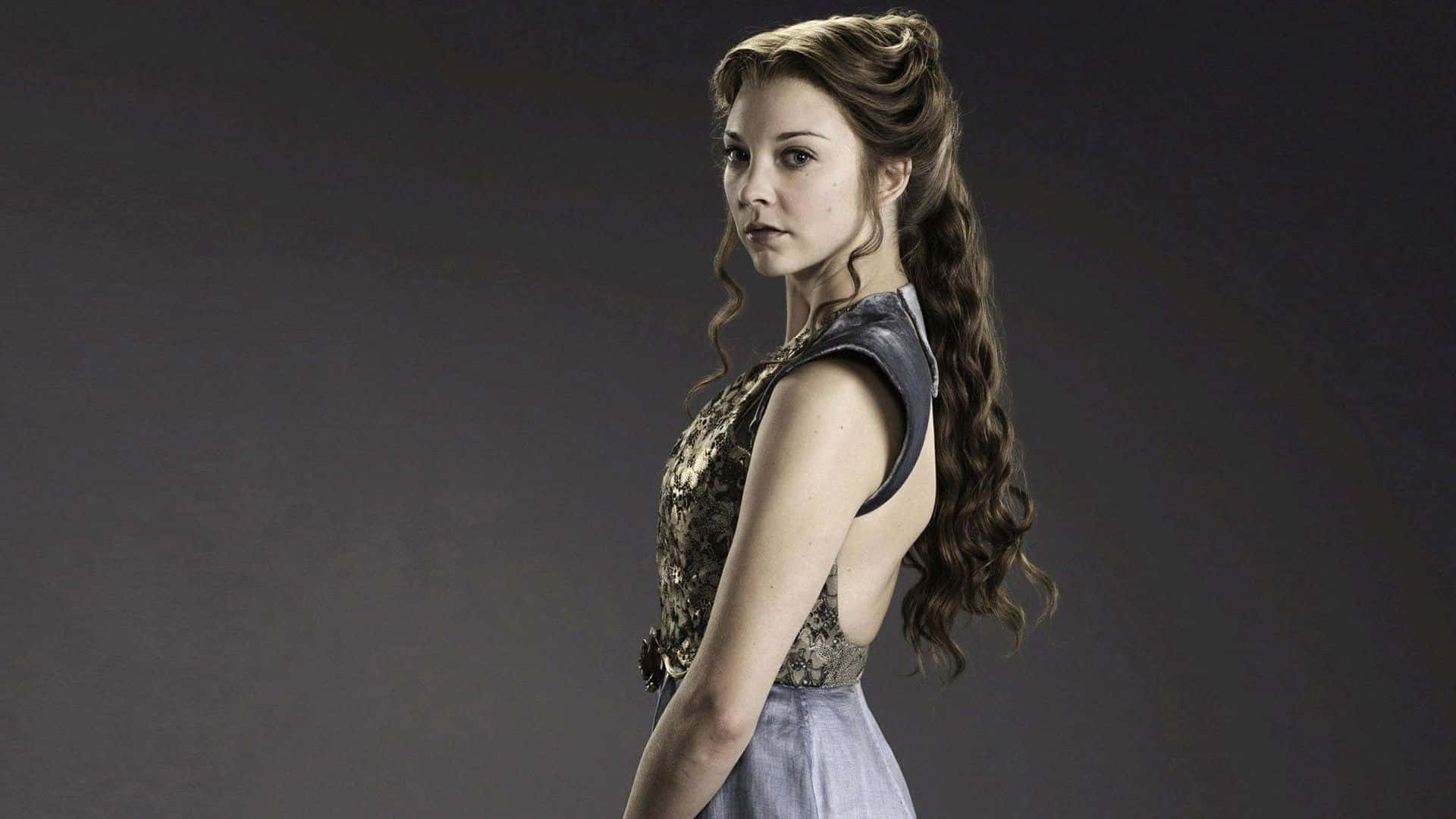 natalie dormer 桌布 壁紙 — 一位長波浪側辮女子，身穿質感上衣和淺藍色裙子，背景為深灰色攝影棚。