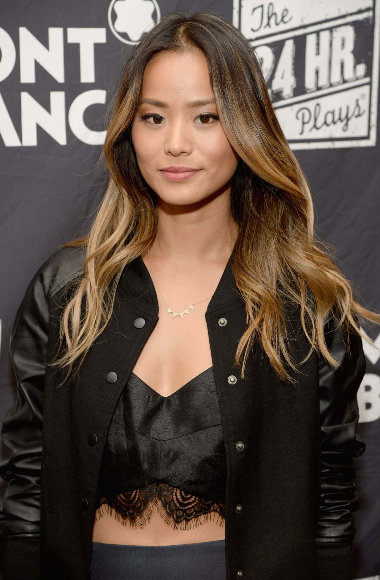 Jamie Chung 桌布 壁紙 — 一位長波浪髮的女性在宣傳活動中穿著黑色短版上衣，外搭黑色飛行員夾克。