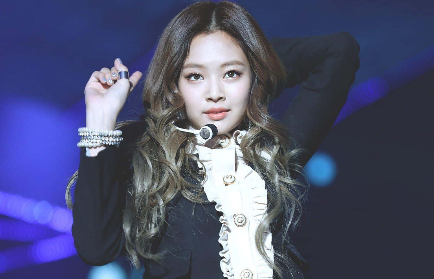 Jennie Kim 桌布 壁紙 — 一位長波浪髮的女表演者在藍色燈光的舞台上擺姿勢，身穿黑白服裝並佩戴珍珠手鐲。